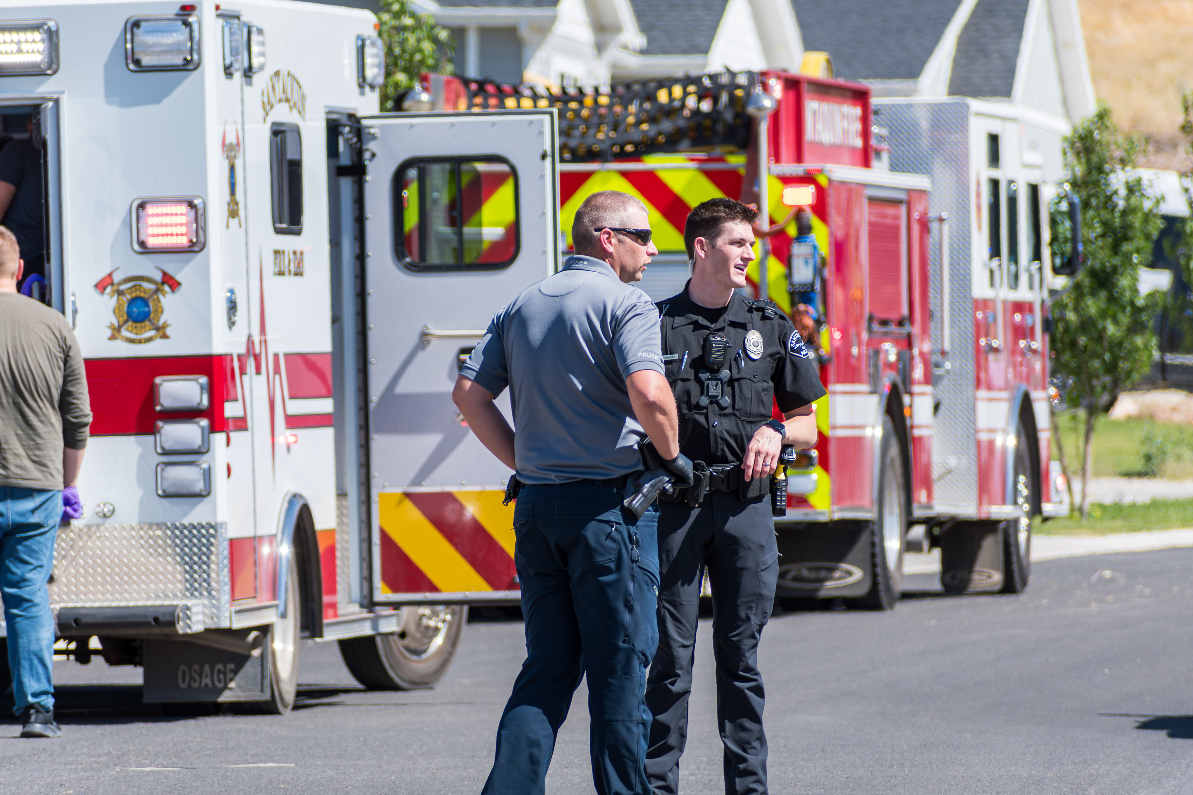 Santaquin, Utah, USA — September 1, 2025: Two police officers confer in front of a fire truck and ambulance on a residential street following a fall-related emergency. 