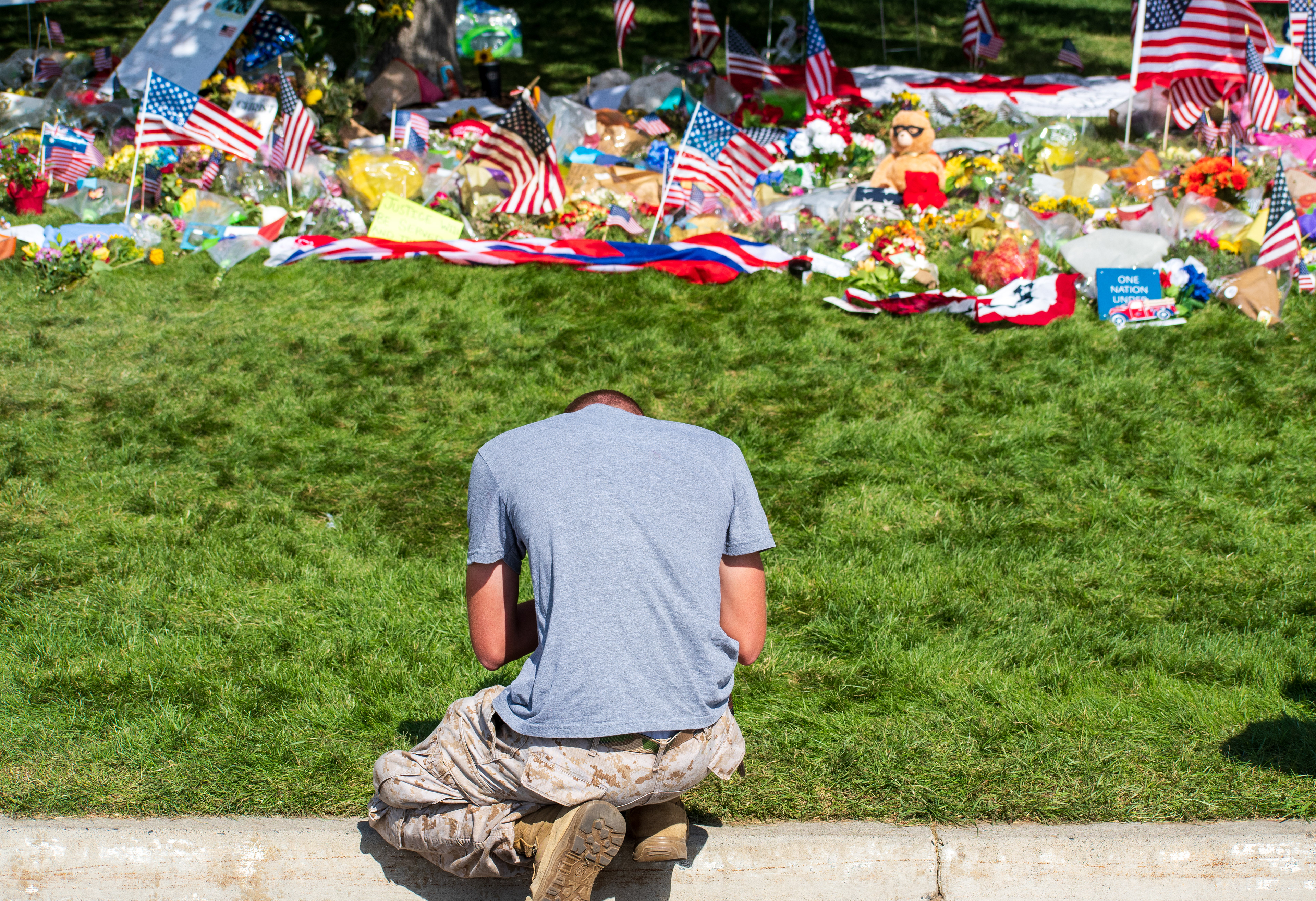 OREM, UTAH – SEPTEMBER 15, 2025: A person kneels at a memorial site for Charlie Kirk on the campus of Utah Valley University. The tribute includes American flags, flowers, stuffed animals, and handwritten signs arranged around a tree near a sidewalk. Vehicles and other individuals are visible in the background. © Charles‑McClintock Wilson / ZUMA Press