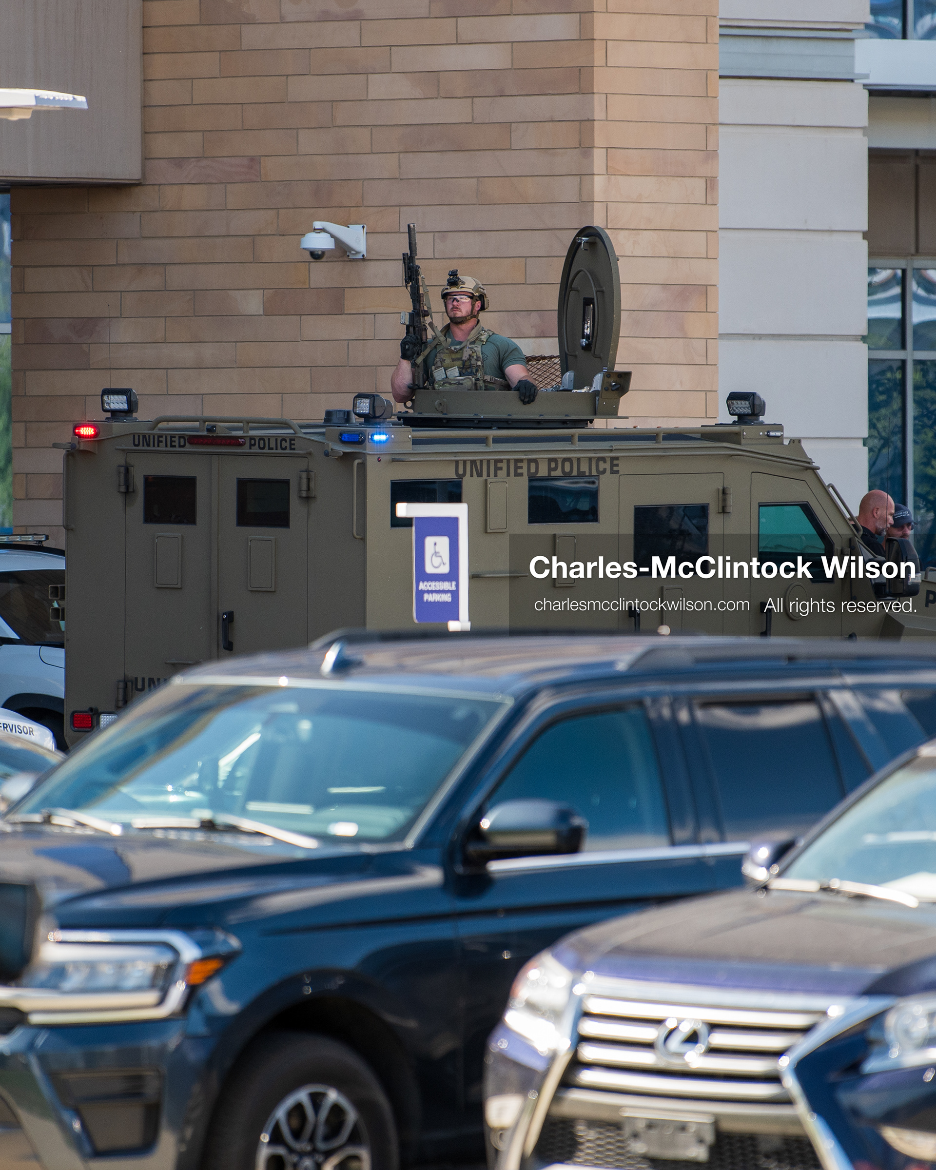 An armed law enforcement officer stands inside the roof turret hatch of an armored tactical vehicle positioned near the emergency department entrance at Intermountain Medical Center in Murray, Utah, United States, on August 17, 2026. Multiple regional police agencies secured the hospital perimeter as a safety precaution after shooting victims were admitted following a fatal shootout outside a funeral service in nearby Kearns. (Photo by Charles-McClintock Wilson/NurPhoto)