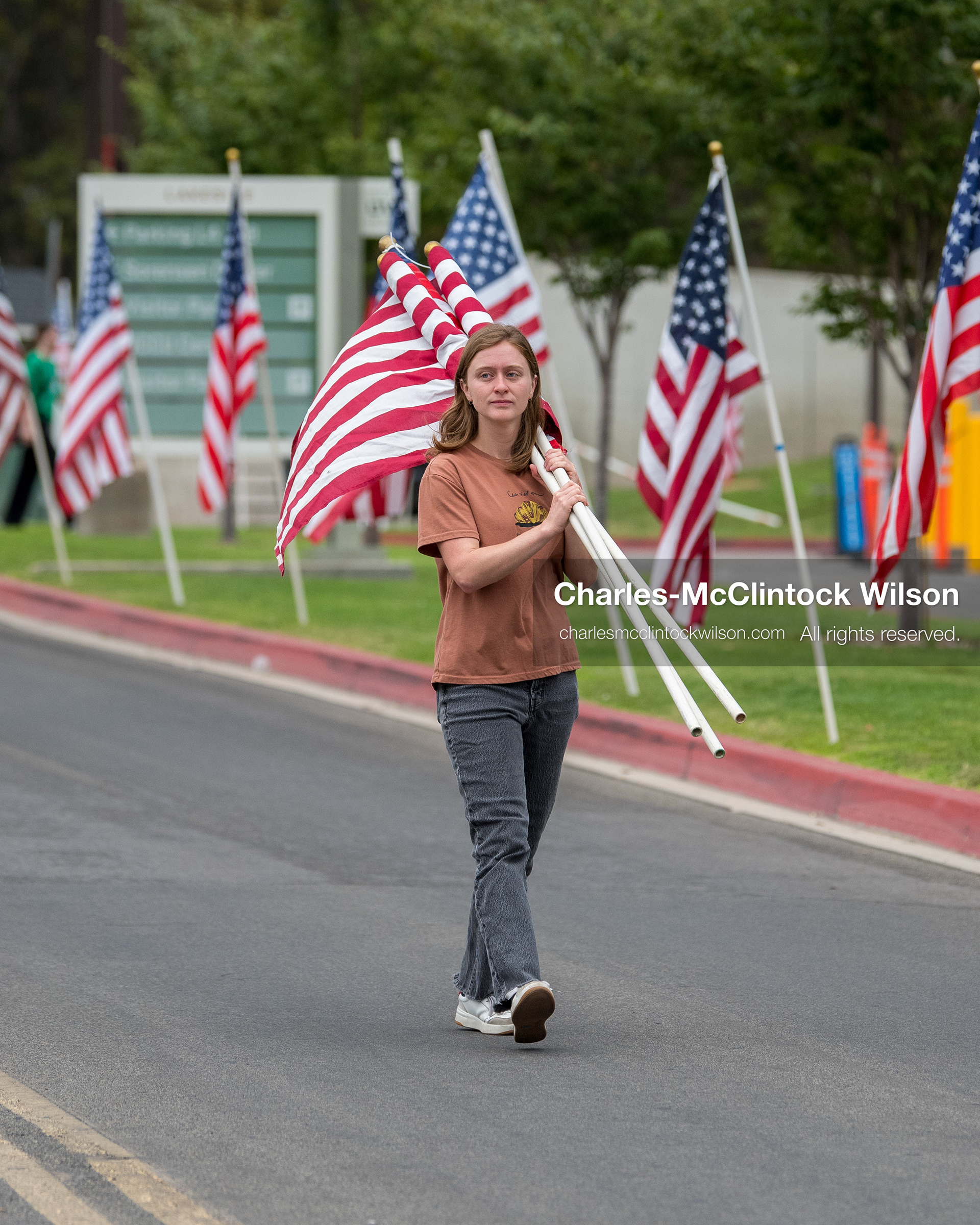 A volunteer carries an American flag along a concrete walkway outside the UCCU Center at Utah Valley University in Orem, Utah, on Wednesday, July 29, 2026. The flags were placed to line the path for community members attending the public memorial ceremony for Provo Fire Captain Spencer Long and his family. (Photo by Charles-McClintock Wilson/Sipa USA)