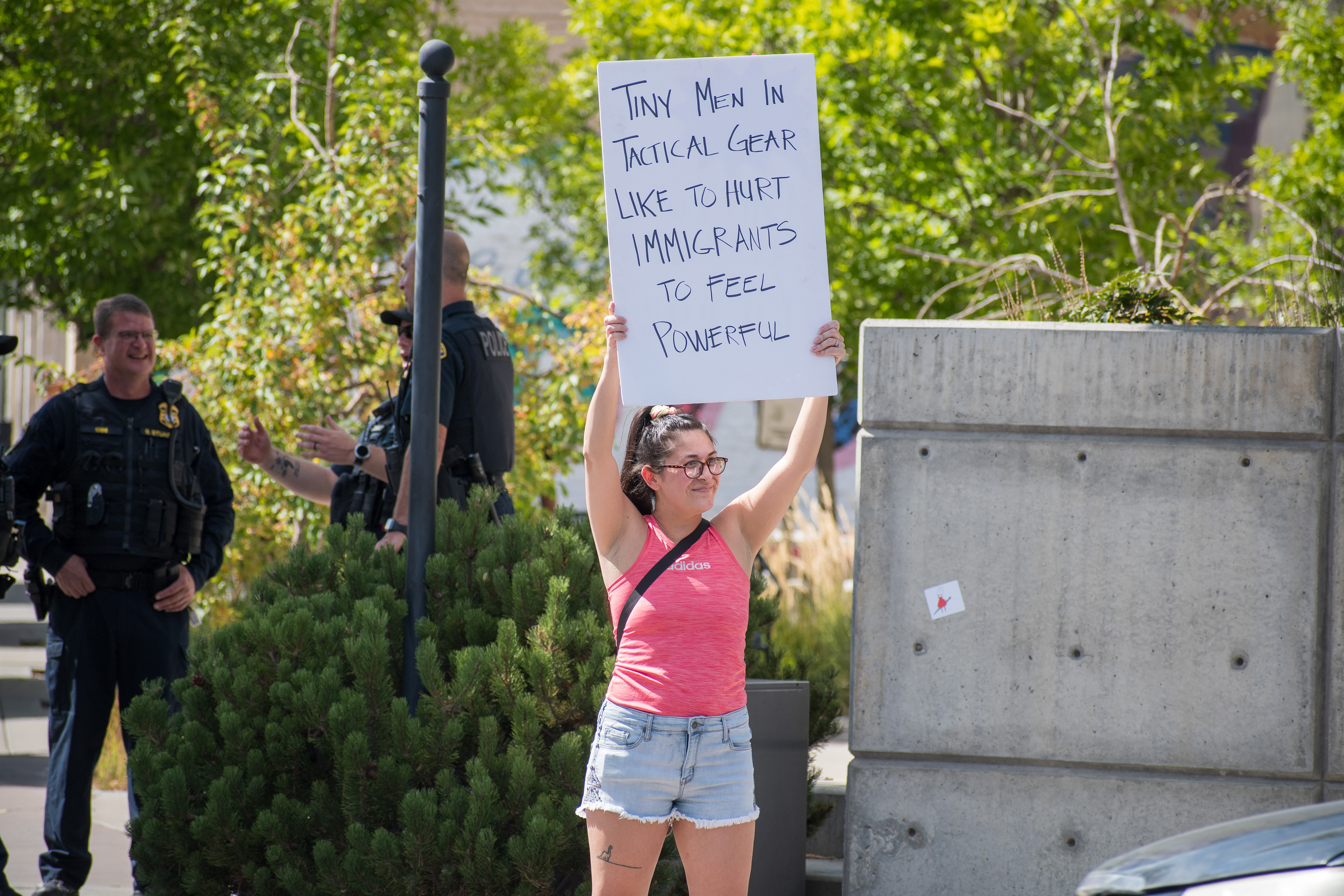 September 15, 2025 – Provo, Utah, United States: A demonstrator holds a sign reading “Tiny Men In Tactical Gear Like To Hurt IMMIGRANTS To Feel Powerful” outside the Utah Valley Convention Center during a protest against the Department of Homeland Security career expo. A police officer in tactical gear stands nearby as protestors voice opposition to federal enforcement practices. Photograph by Charles‑McClintock Wilson / ZUMA Press Wire