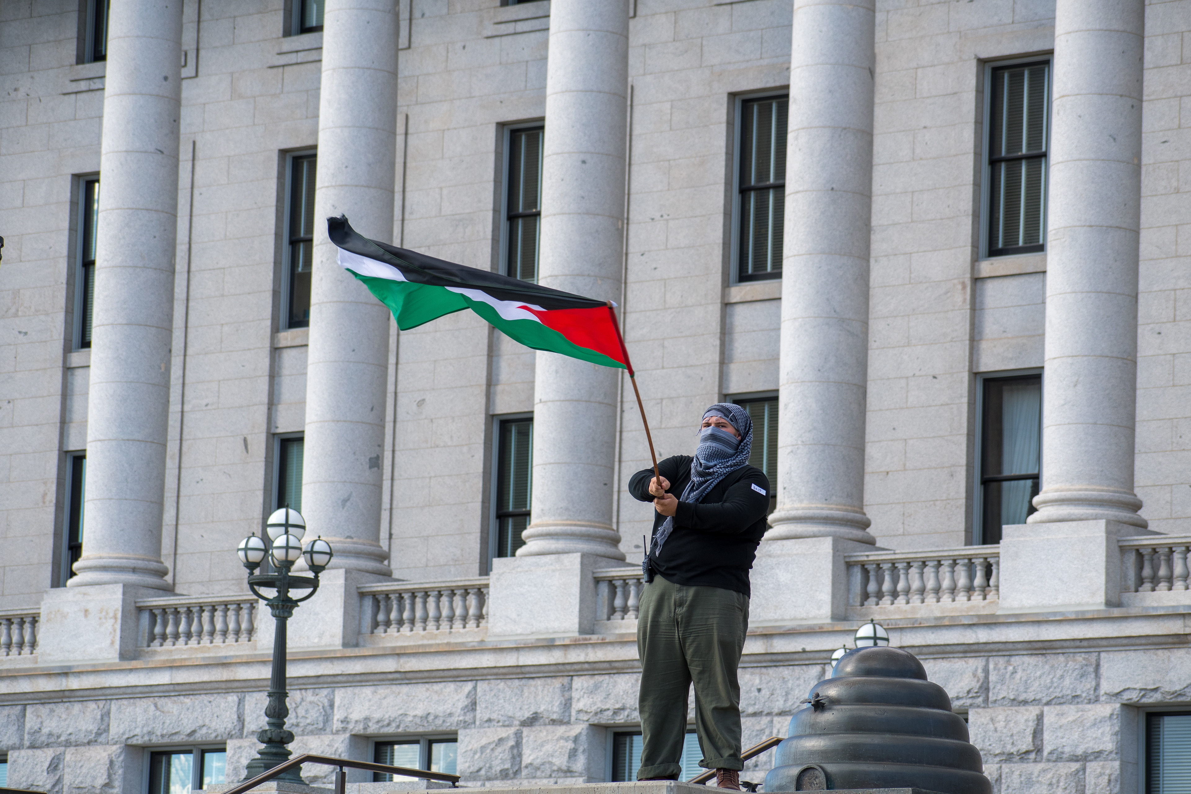 October 10, 2025, Salt Lake City, Utah, USA: A demonstrator stands on a raised platform outside the Utah State Capitol during the Free Palestine Rally. The participant waves a Palestinian flag while wearing a face covering and casual clothing. (Credit Image: © Charles-McClintock Wilson/ZUMA Press Wire)