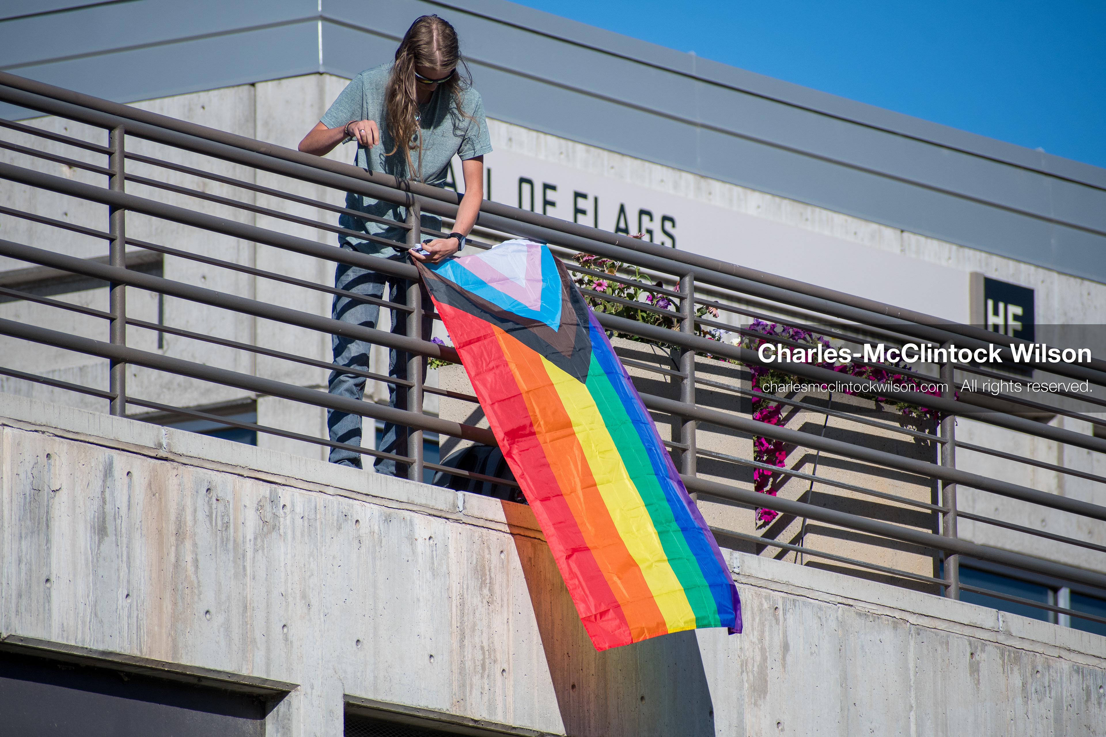 September 10, 2025, Orem, Utah, USA: A lone individual displays a Progress Pride flag from an elevated structure overlooking the Fountain Courtyard at Utah Valley University, where conservative activist Charlie Kirk was speaking as part of his American Comeback Tour. The flag’s presence marked a moment of symbolic contrast amid a politically charged atmosphere. Kirk was fatally shot moments later during the public Q&A session, prompting national scrutiny of campus security protocols and institutional response. (Credit Image: © Charles‑McClintock Wilson/ZUMA Press Wire)