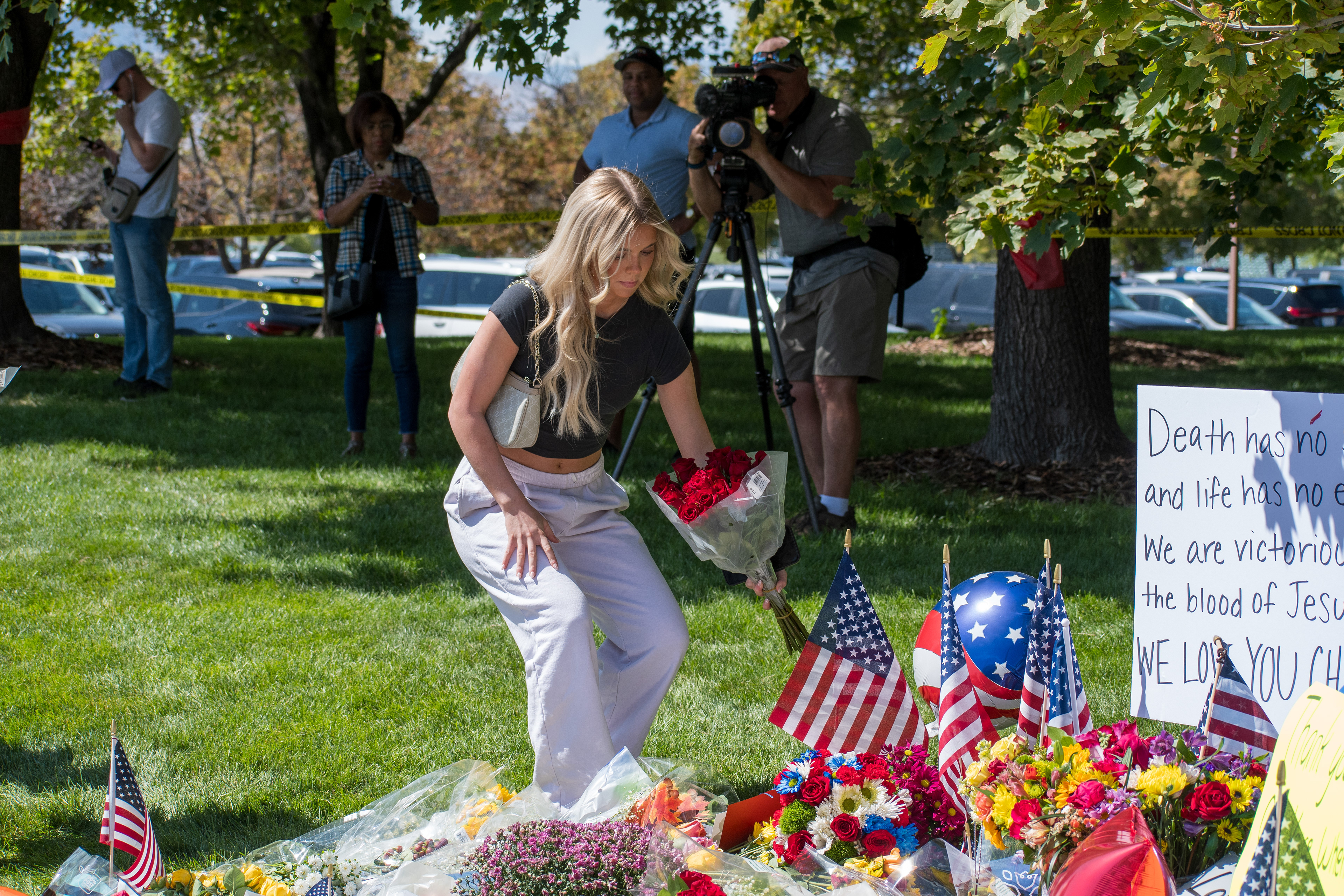 OREM, UTAH – SEPTEMBER 12, 2025: A woman kneels to place flowers at a memorial site for Charlie Kirk near Utah Valley University. Surrounded by bouquets, American flags, and fellow mourners, the tribute reflects a moment of quiet remembrance and communal grief. © Charles‑McClintock Wilson / ZUMA Press