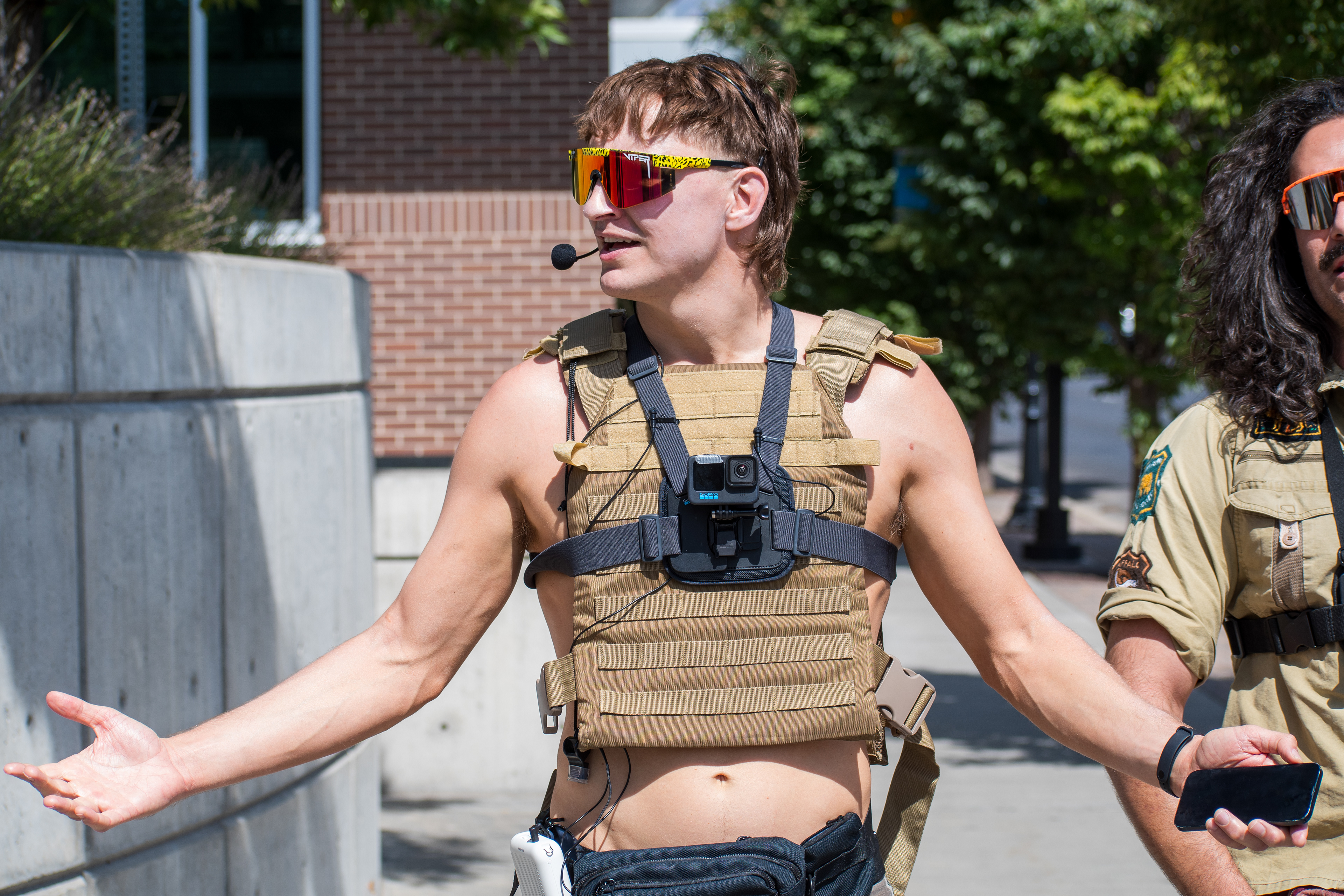 September 15, 2025 – Provo, Utah, United States: A demonstrator wearing tactical gear gestures emphatically outside the Utah Valley Convention Center during a protest against the Department of Homeland Security career expo. The individual’s vest-mounted camera and headset microphone suggest a performative or media-driven presence amid civic dissent. Photograph by Charles‑McClintock Wilson / ZUMA Press Wire