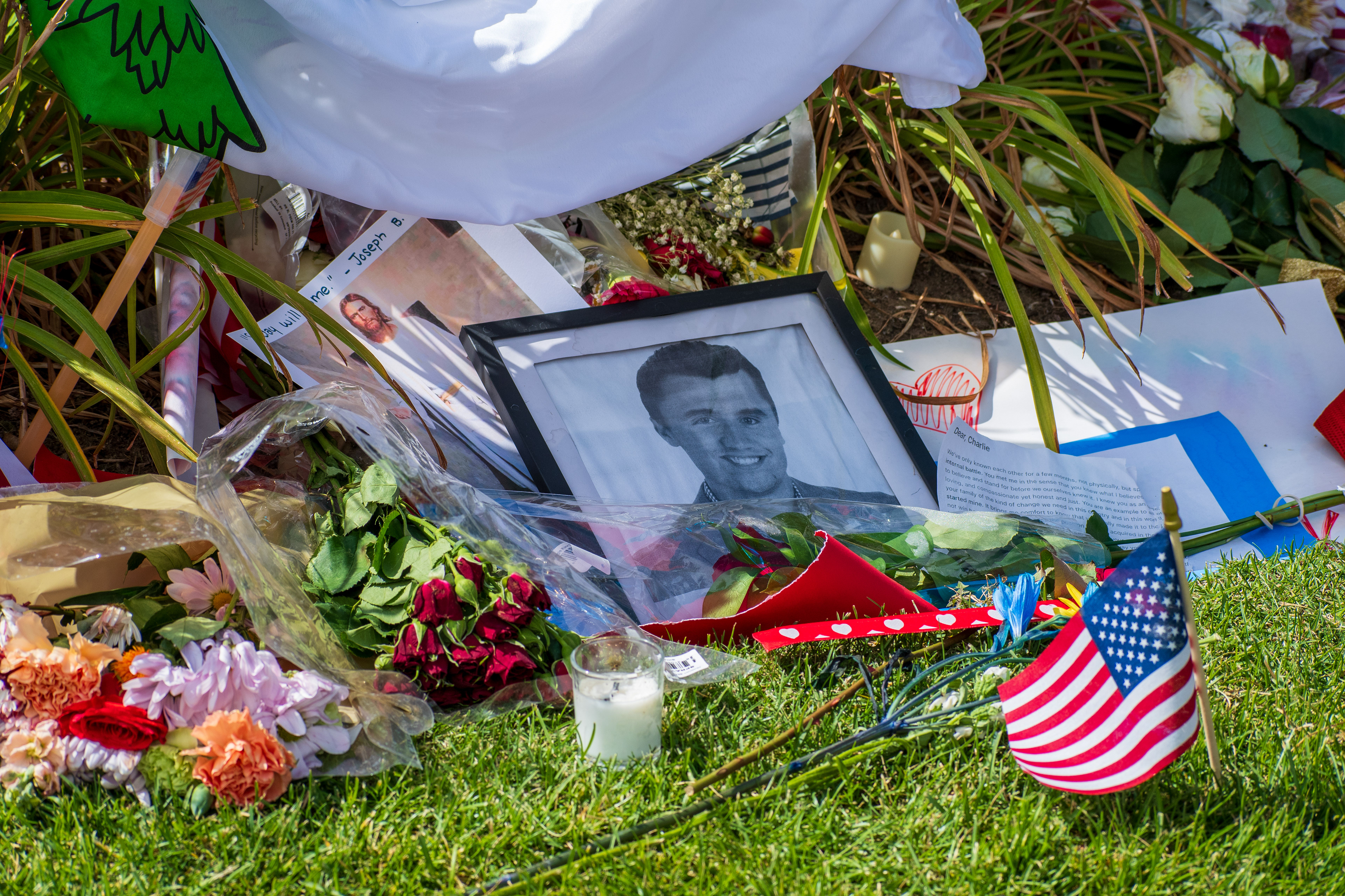 OREM, UTAH – SEPTEMBER 12, 2025: A framed black-and-white photograph is surrounded by American flags, flowers, handwritten notes, and personal tributes at a memorial site for Charlie Kirk outside Timpanogos Regional Hospital. Red and white roses, a bouquet wrapped in plastic, and a white cloth with green and red designs are arranged around the image. © Charles‑McClintock Wilson / ZUMA Press