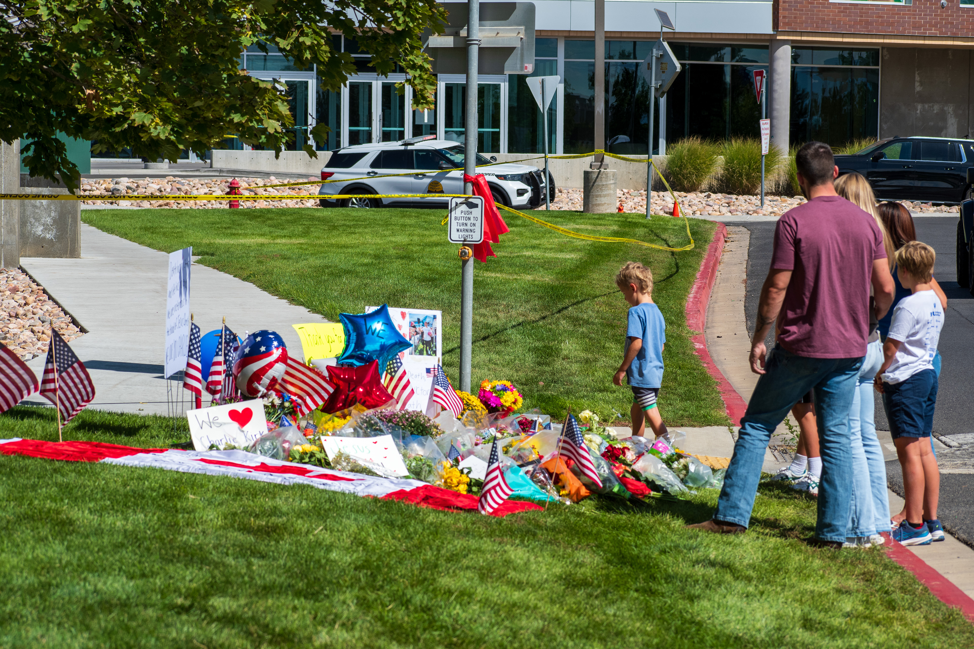 OREM, UTAH – SEPTEMBER 12, 2025: Families gather at a memorial site for Charlie Kirk on the campus of Utah Valley University. The tribute includes American flags, balloons, flowers, and handwritten posters arranged near a building entrance. © Charles‑McClintock Wilson / ZUMA Press