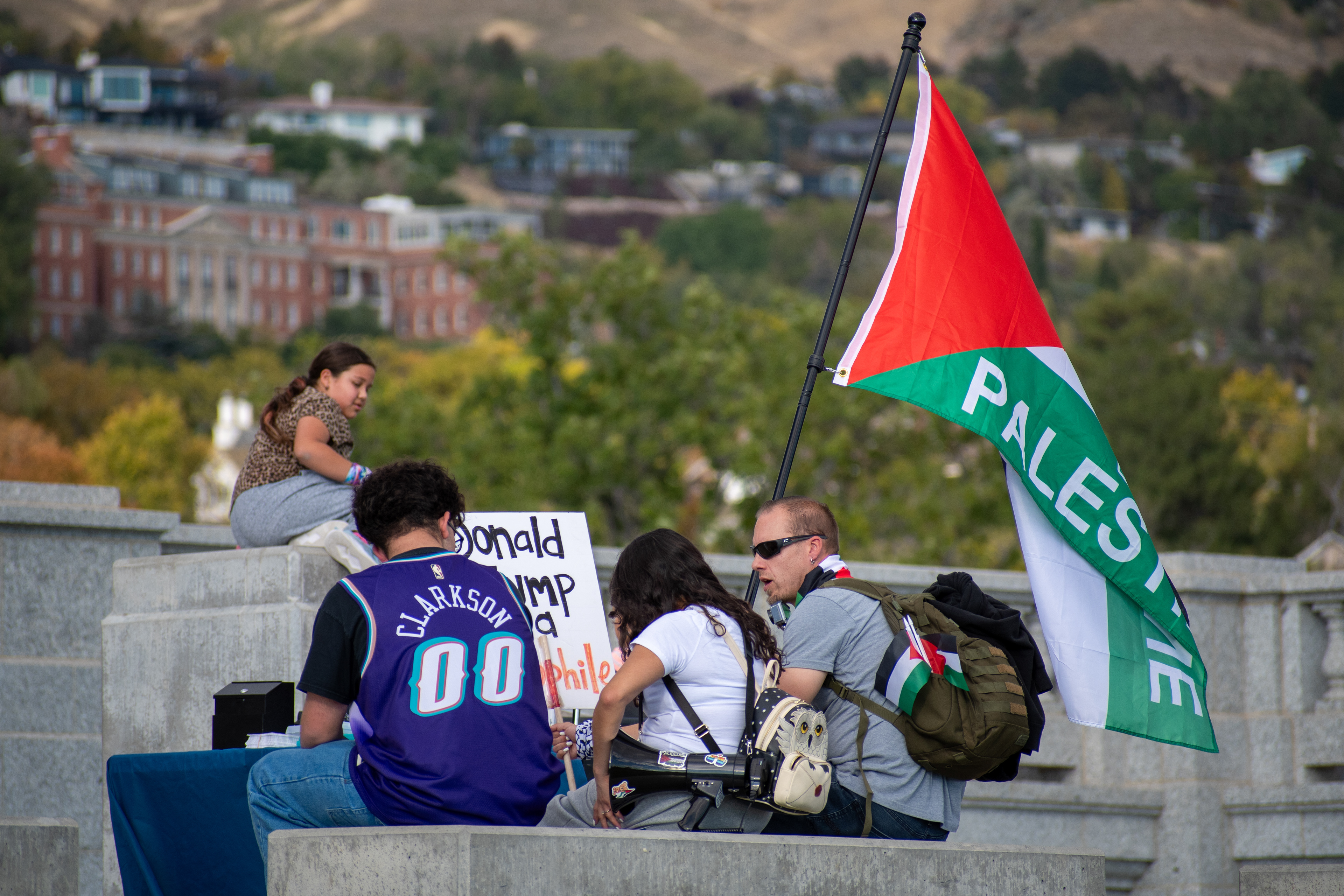 October 10, 2025, Salt Lake City, Utah, USA: Demonstrators sit on a concrete bench during the Free Palestine Rally organized in front of the Utah State Capitol. Participants display flags and signs as city buildings and mountain peaks frame the background. (Credit Image: © Charles-McClintock Wilson/ZUMA Press Wire)