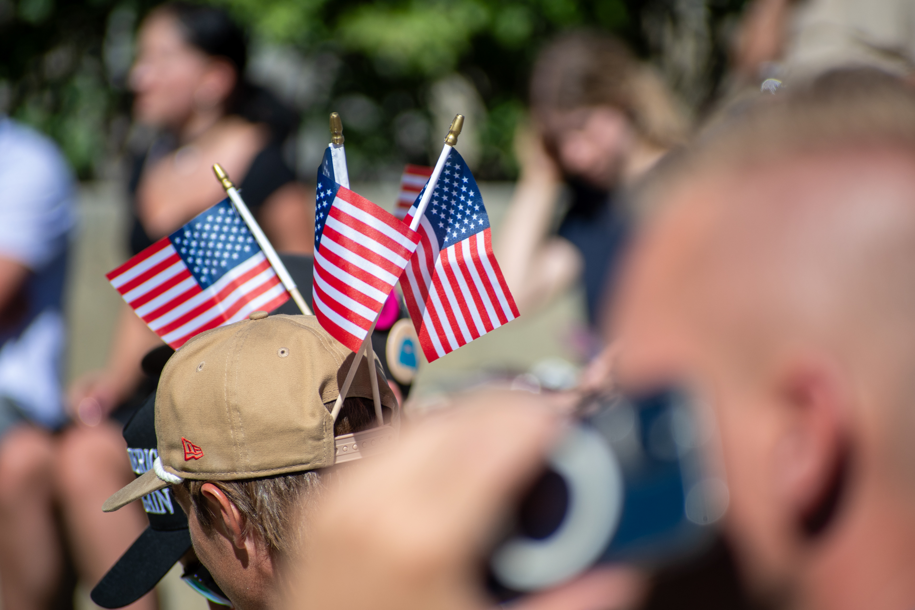 OREM, UTAH – SEPTEMBER 10, 2025: Attendees gather outdoors at Utah Valley University during the opening stop of the American Comeback Tour. Two individuals wear caps adorned with small American flags, reflecting a moment of personal expression and quiet symbolism. The image captures the warmth, texture, and communal presence that shaped the event’s atmosphere. © Charles-McClintock Wilson / ZUMA Press