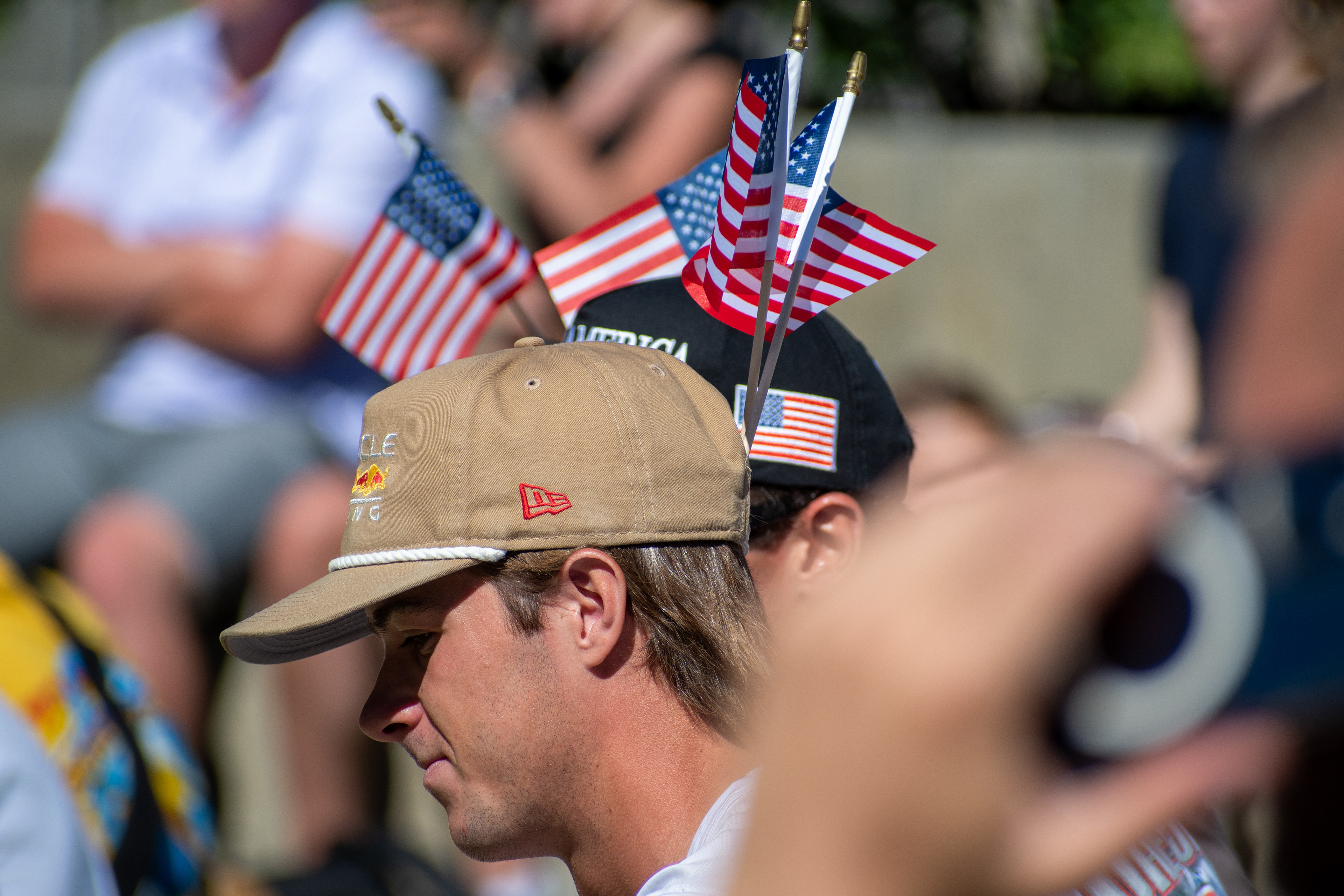 OREM, UTAH – SEPTEMBER 10, 2025: Attendees gather outdoors at Utah Valley University during the opening stop of the American Comeback Tour. Two individuals wear caps adorned with small American flags, reflecting a moment of personal expression and quiet symbolism. The image captures the warmth, texture, and communal presence that shaped the event’s atmosphere. © Charles-McClintock Wilson / ZUMA Press
