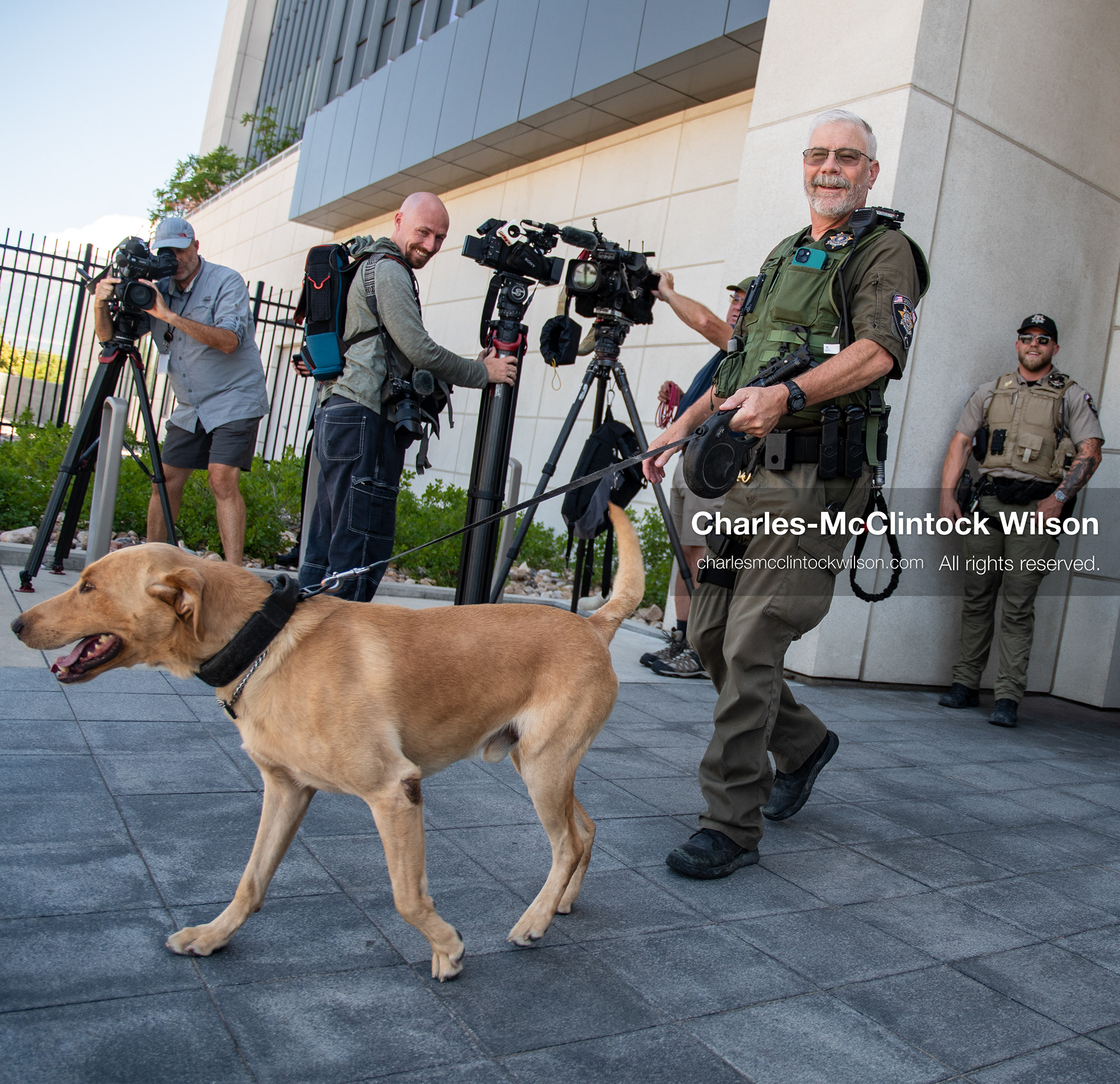 July 8, 2026, Provo, Utah, USA: A law enforcement officer leads a K‑9 unit outside the Fourth District Court in Provo during the third day of the preliminary hearing in the Tyler Robinson case. Members of the media and security personnel stand nearby as prosecutors continue presenting evidence to determine whether probable cause exists for the case to proceed to trial after Charlie Kirk was fatally shot at Utah Valley University in 2025. (Credit Image: © Charles McClintock Wilson/ZUMA Press Wire)