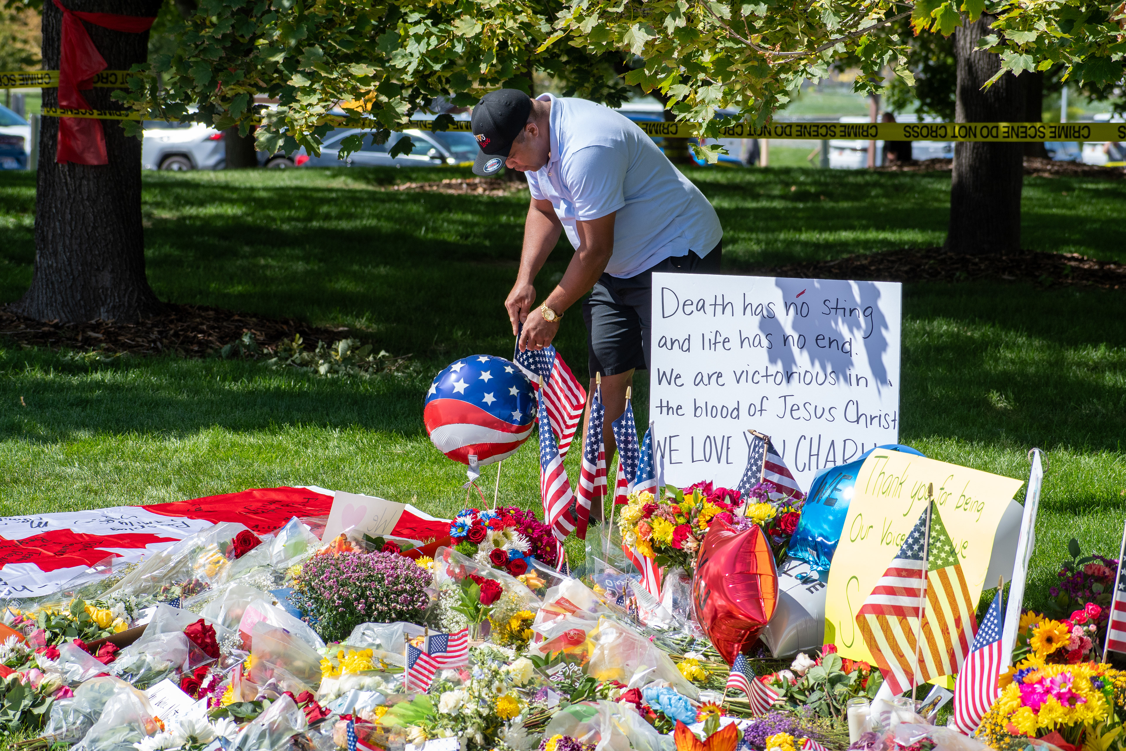 OREM, UTAH – SEPTEMBER 12, 2025: A man places American flags at a memorial site for Charlie Kirk in a shaded park near Utah Valley University. The tribute includes flowers, handwritten posters, and personal items arranged beneath the trees. © Charles‑McClintock Wilson / ZUMA Press