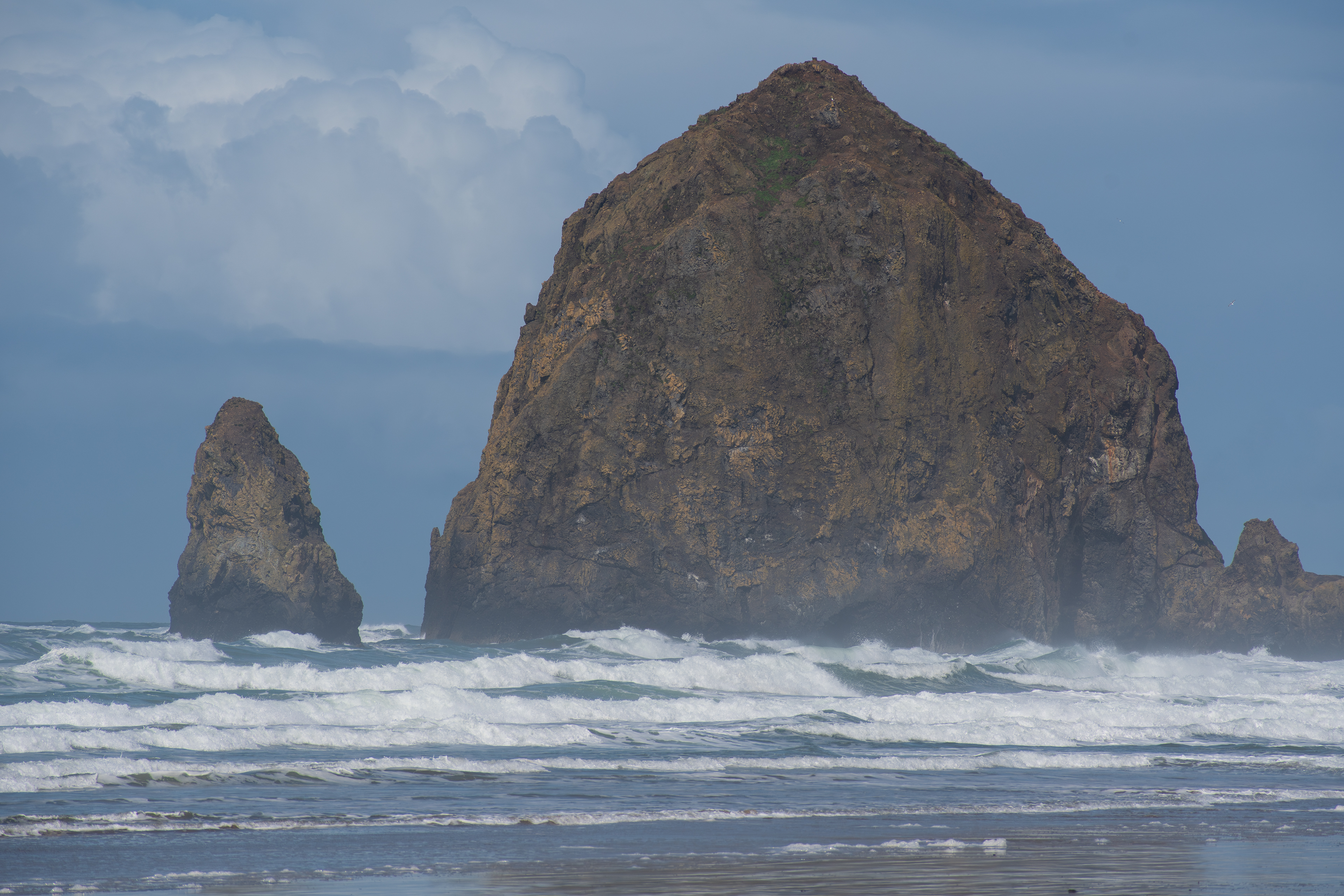 CANNON BEACH, OR, USA - APR 12, 2025: The iconic tall rock formations at Cannon Beach stand against the backdrop of a cloudy sky, creating a dramatic coastal scene along the Pacific Northwest shorelin