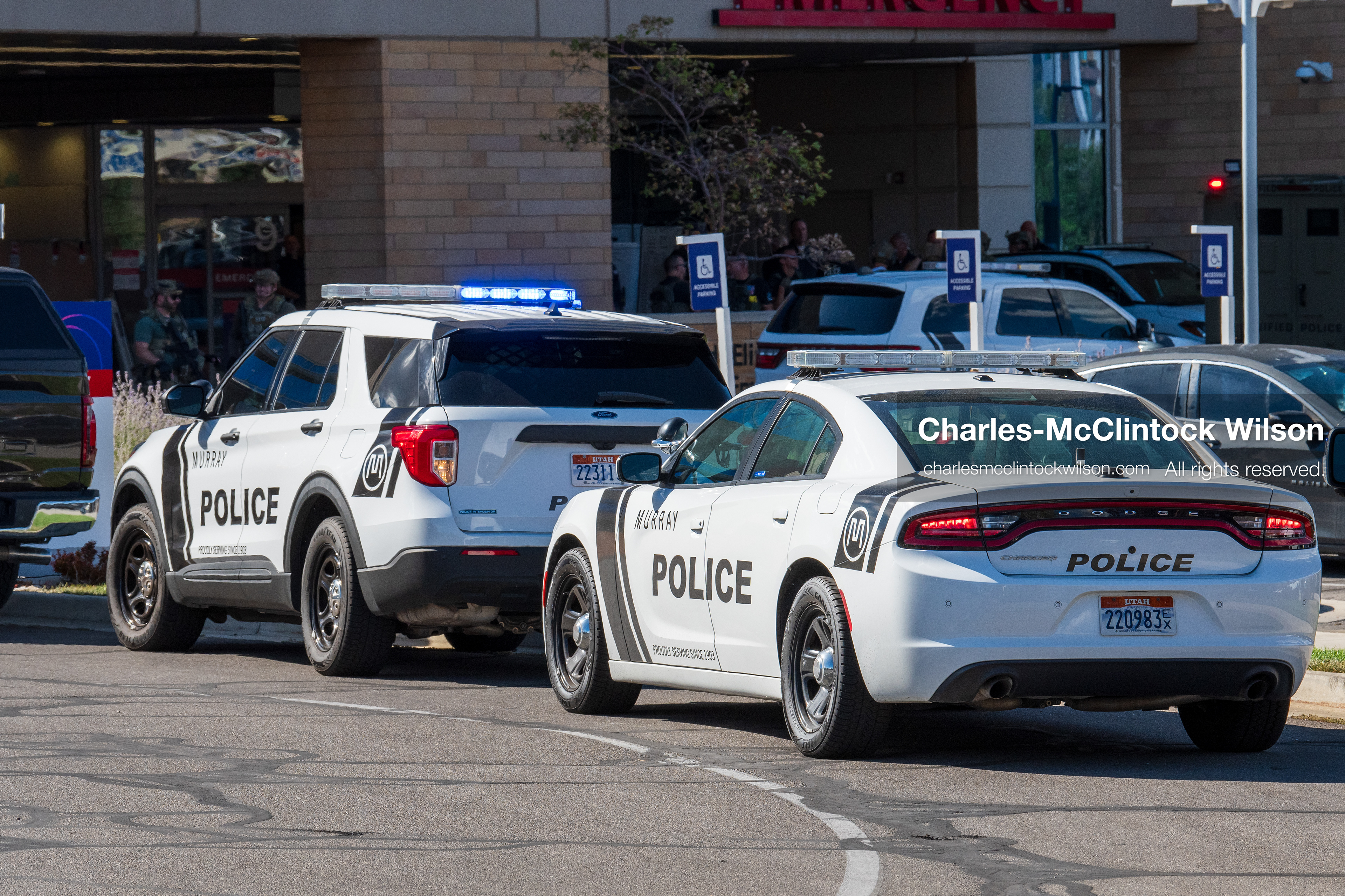 Marked police cruisers with emergency lights flashing sit parked in a line outside the emergency department entrance at Intermountain Medical Center in Murray, Utah, on Monday, August 17, 2026. Multiple regional law enforcement agencies converged to heavily secure the hospital perimeter as a safety precaution after shooting victims arrived from a fatal shootout that erupted outside a funeral service in nearby Kearns earlier that day. (Photo by Charles-McClintock Wilson/Sipa USA)