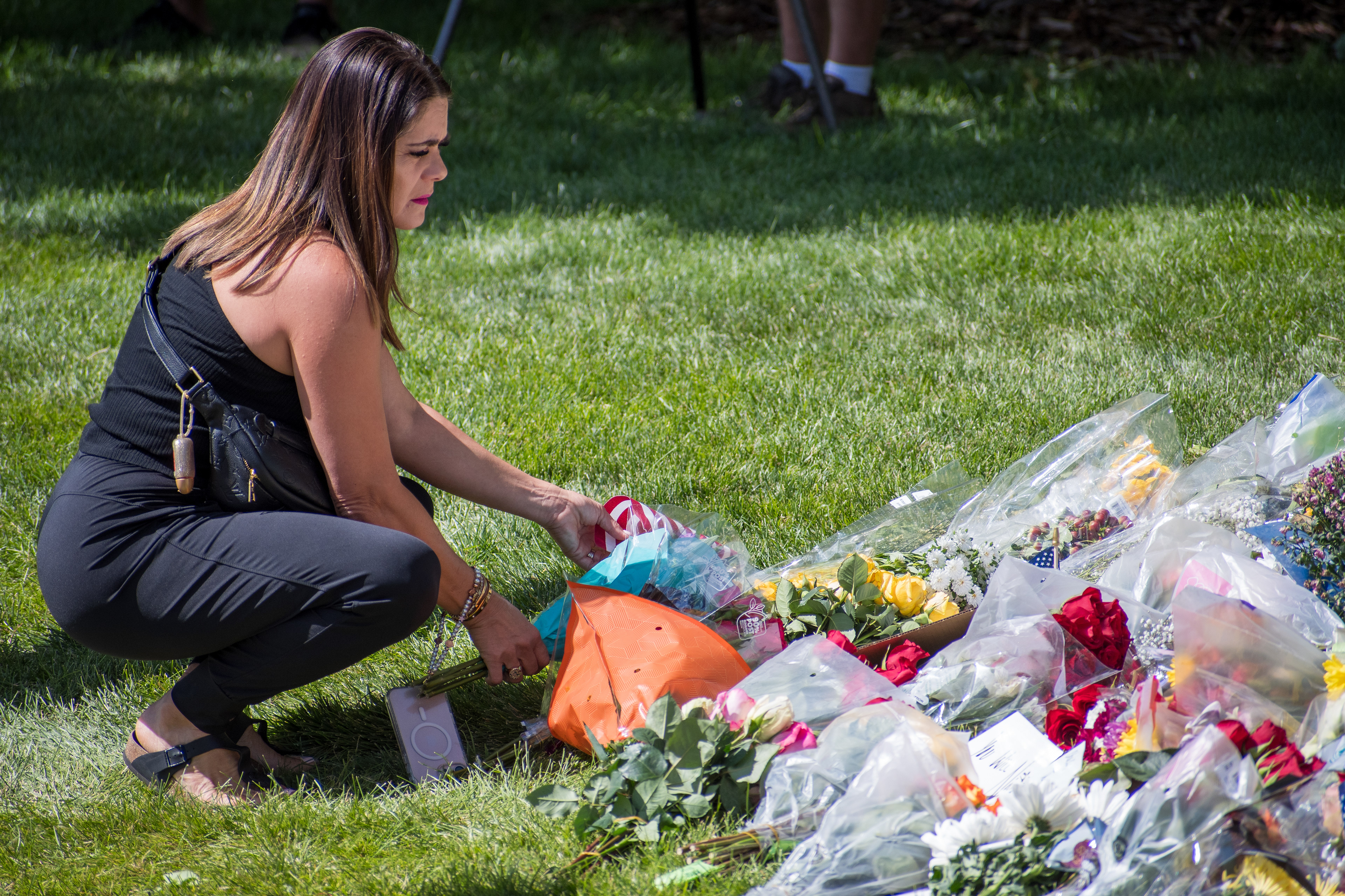 OREM, UTAH – SEPTEMBER 12, 2025: A woman kneels to arrange flowers among a growing collection of floral tributes at a memorial site for Charlie Kirk near Utah Valley University. Wrapped bouquets cover the grass as mourners gather in quiet reflection. © Charles‑McClintock Wilson / ZUMA Press