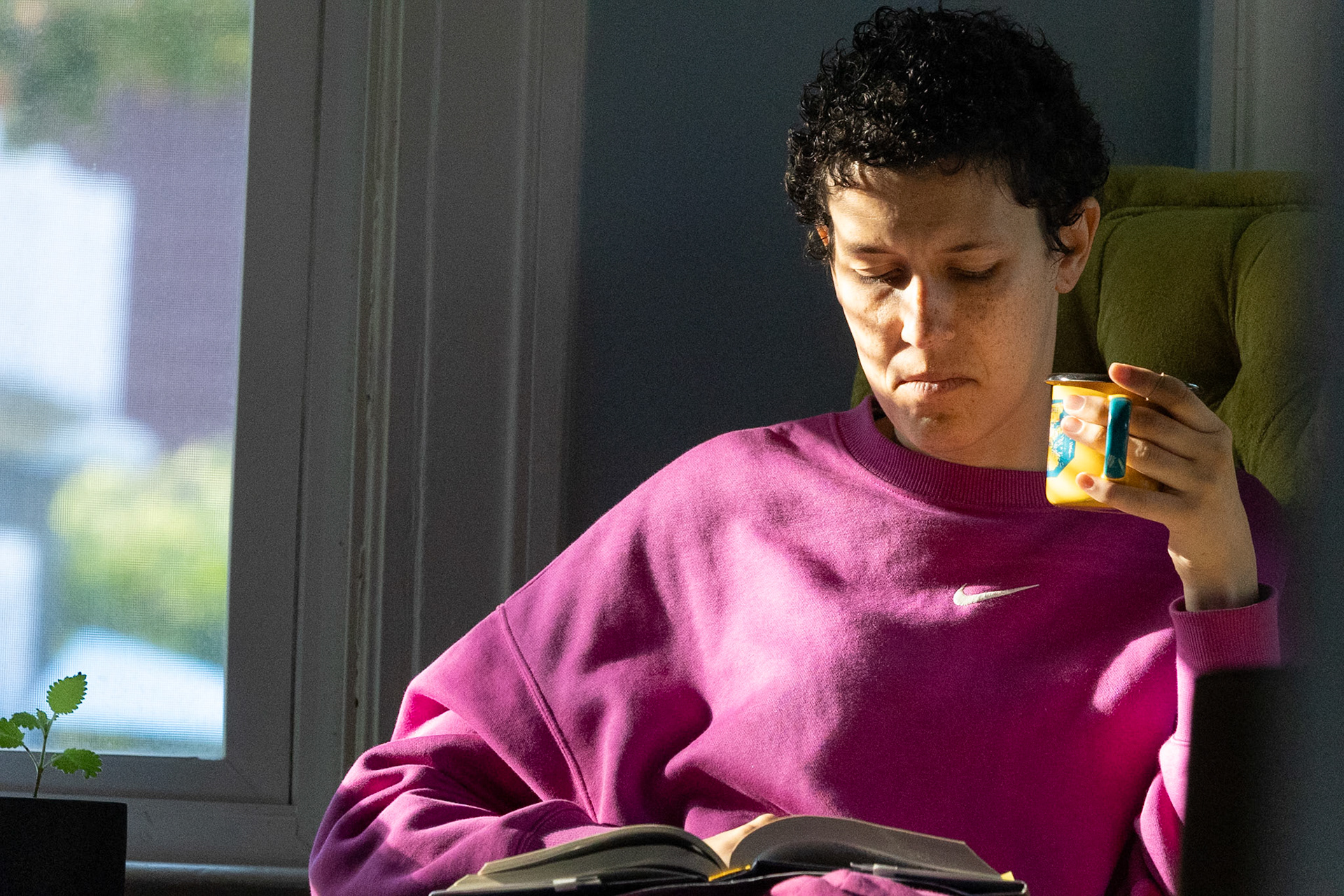 Virginia Combs reads a book in her green chair with her coffee in the morning light in Rochester, NY, on October 4, 2025. Every morning for an hour, she reads a book and sips her coffee to start her day.