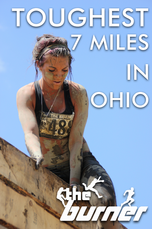 A mud covered woman passes over the top of a large wall obstacle. Text says "Toughest 7 miles in Ohio" with The Burner logo