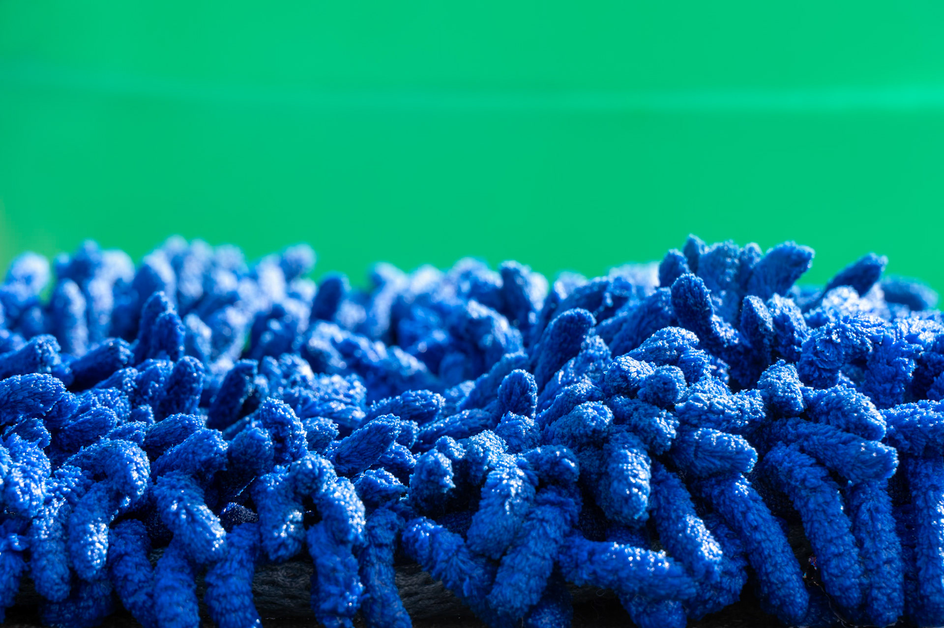 Blue chenille microfiber car wash sponge against a green bucket