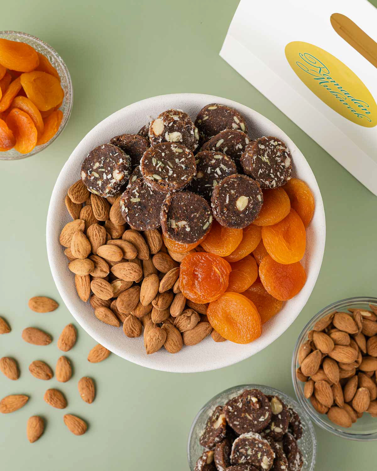 Schaaltje met amandelen, dadels, cacaokoekjes en abrikozen naast een Ramadan Mubarak tas.
