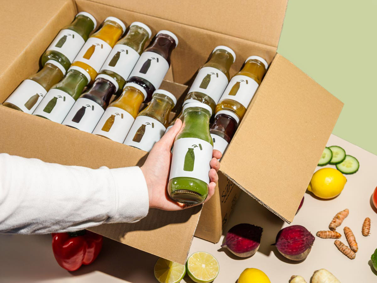 A box of green juices with a hand, made in Amsterdam.
