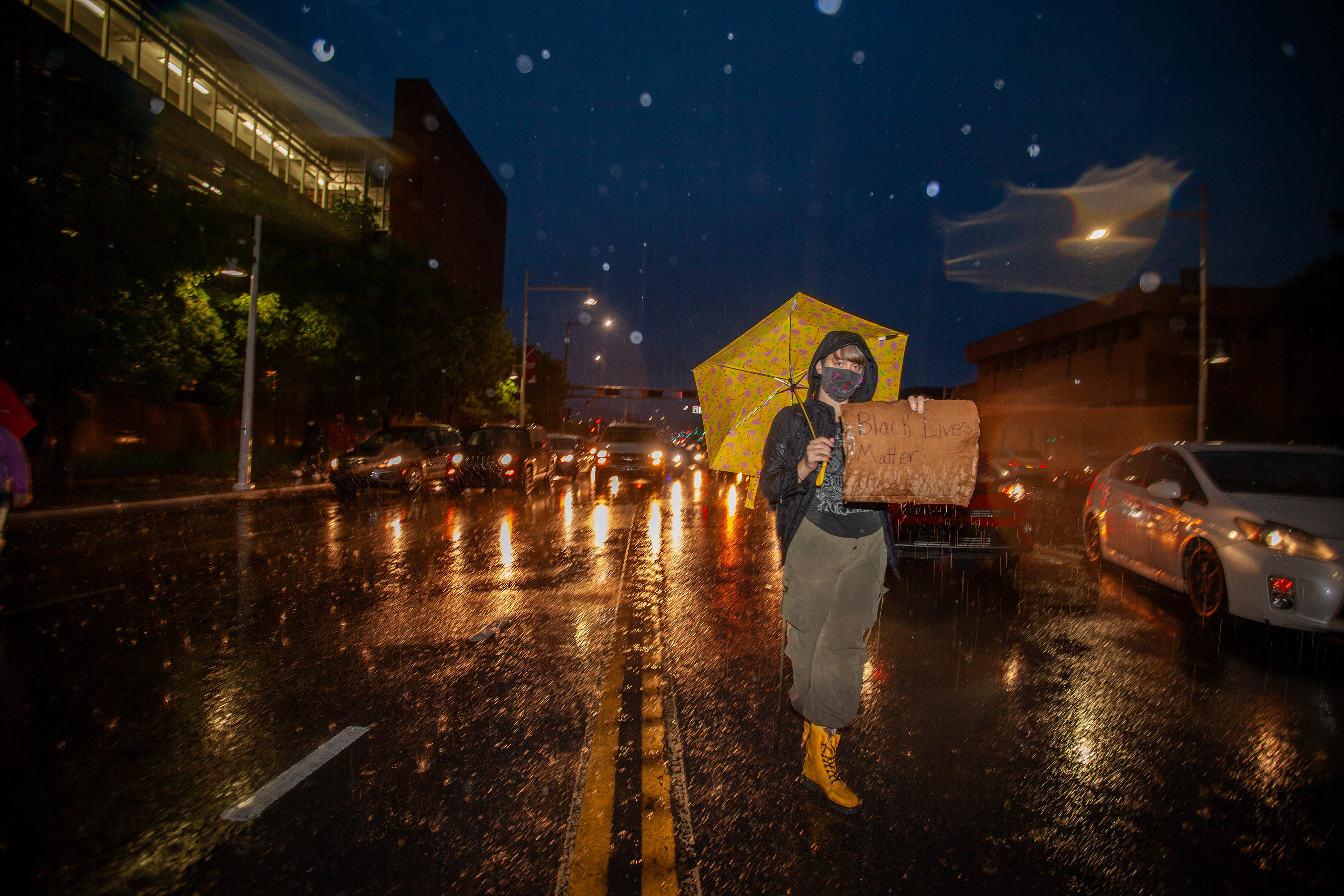 A lone protester stands resilient in the rain, a sign in hand calling for systemic change, amidst nationwide protests sparked by George Floyd's death, June 2020.