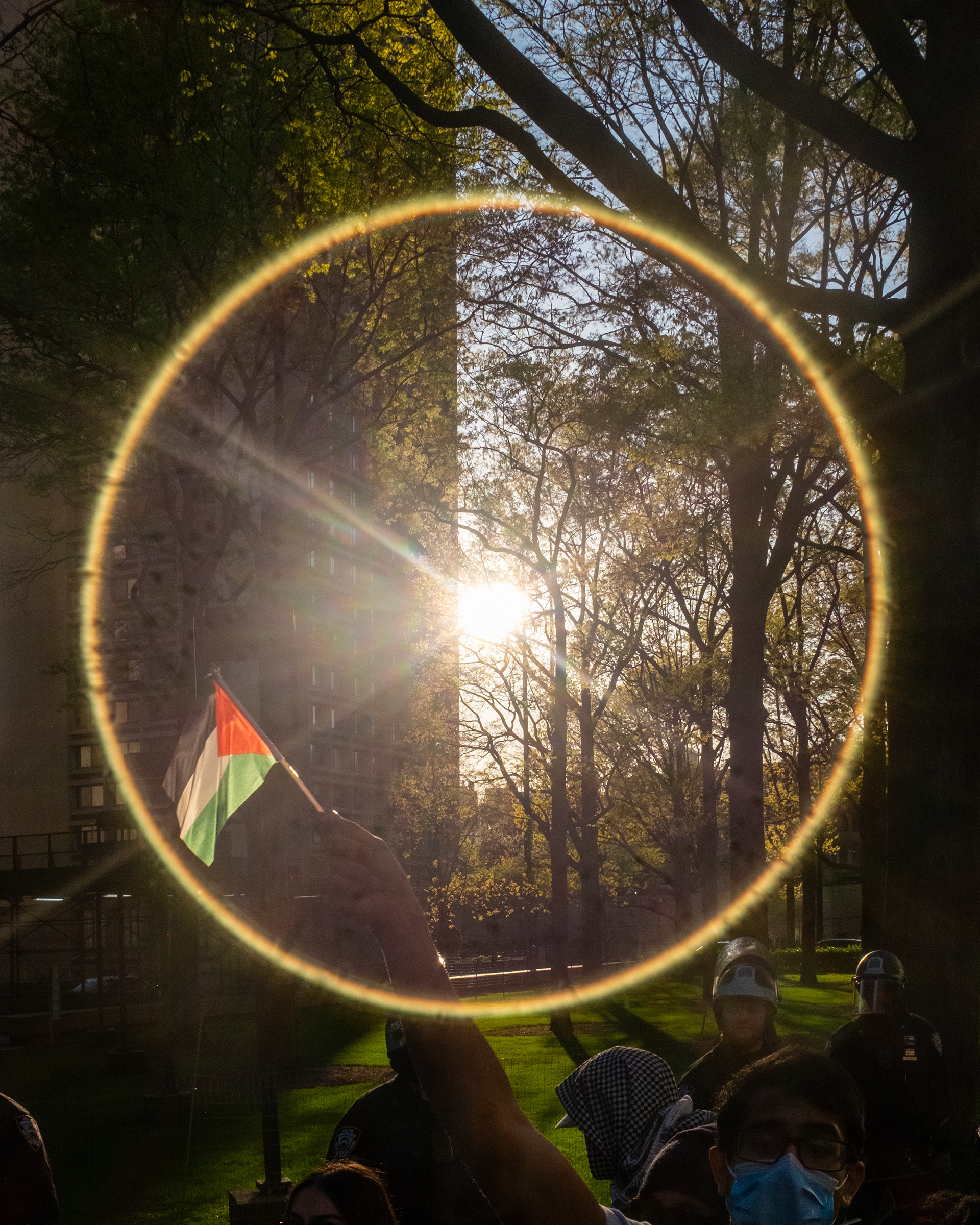 A protester waves a Palestinian flag during a late afternoon demonstration on April 26 at the NYU John A. Paulson Center, New York City. The protest against the Israel-Hamas war draws police oversight as officers in riot gear, including Officer Chrisova Kouimanis, prepare to clear the area.
