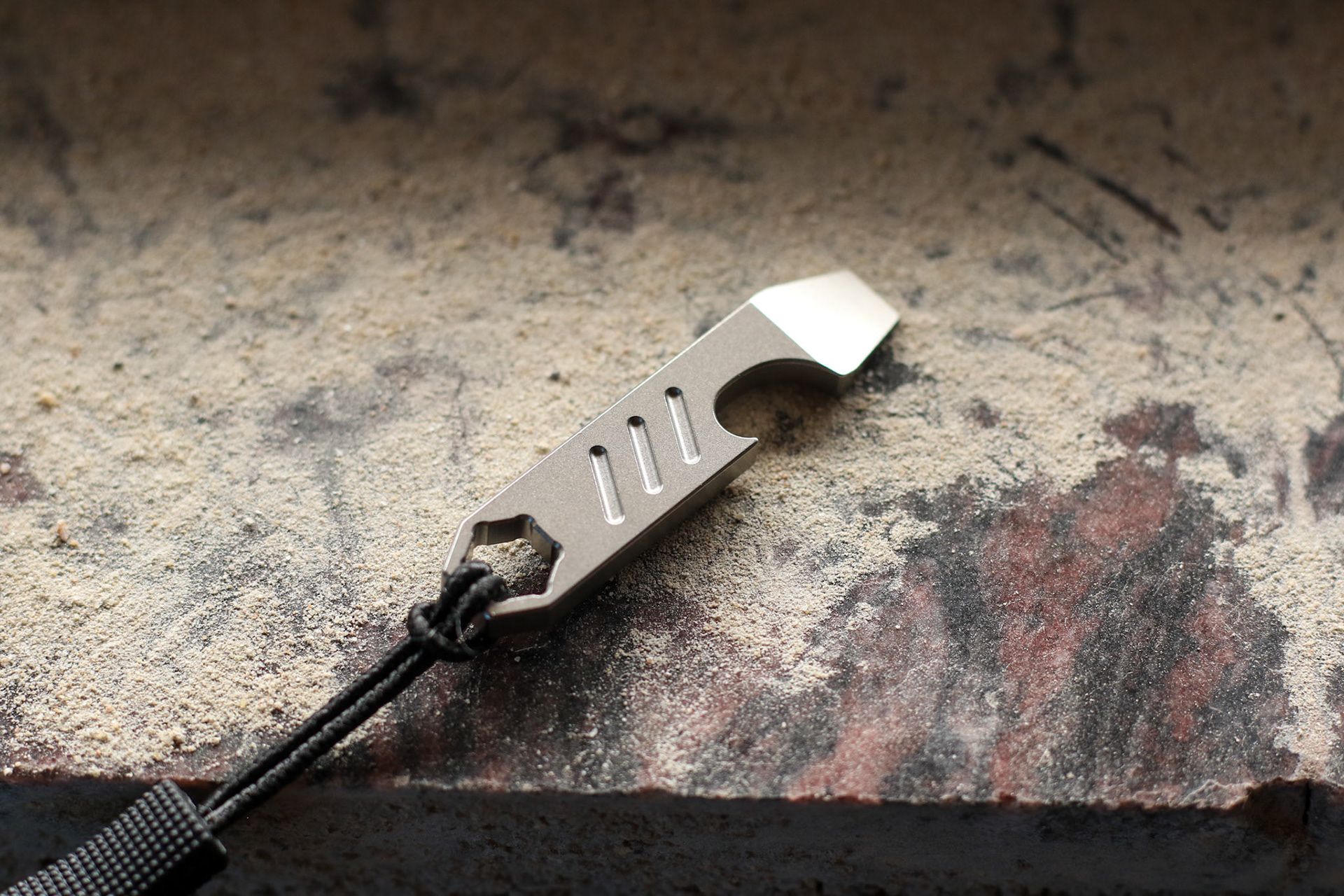 Titanium prybar resting on granite slab among dust with lanyard attached