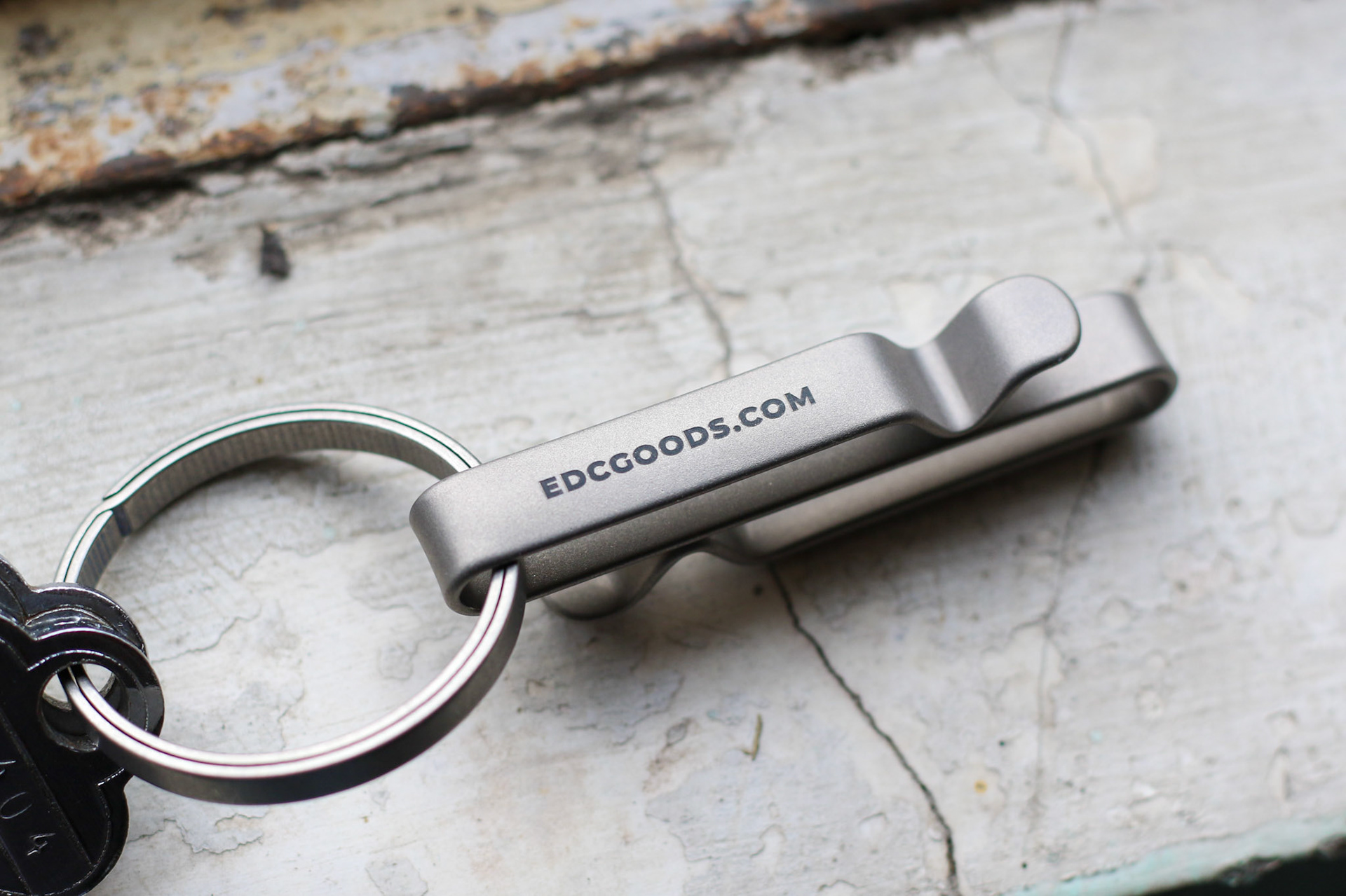 Titanium belt clip lying on concrete with keys attached to the titanium keyring