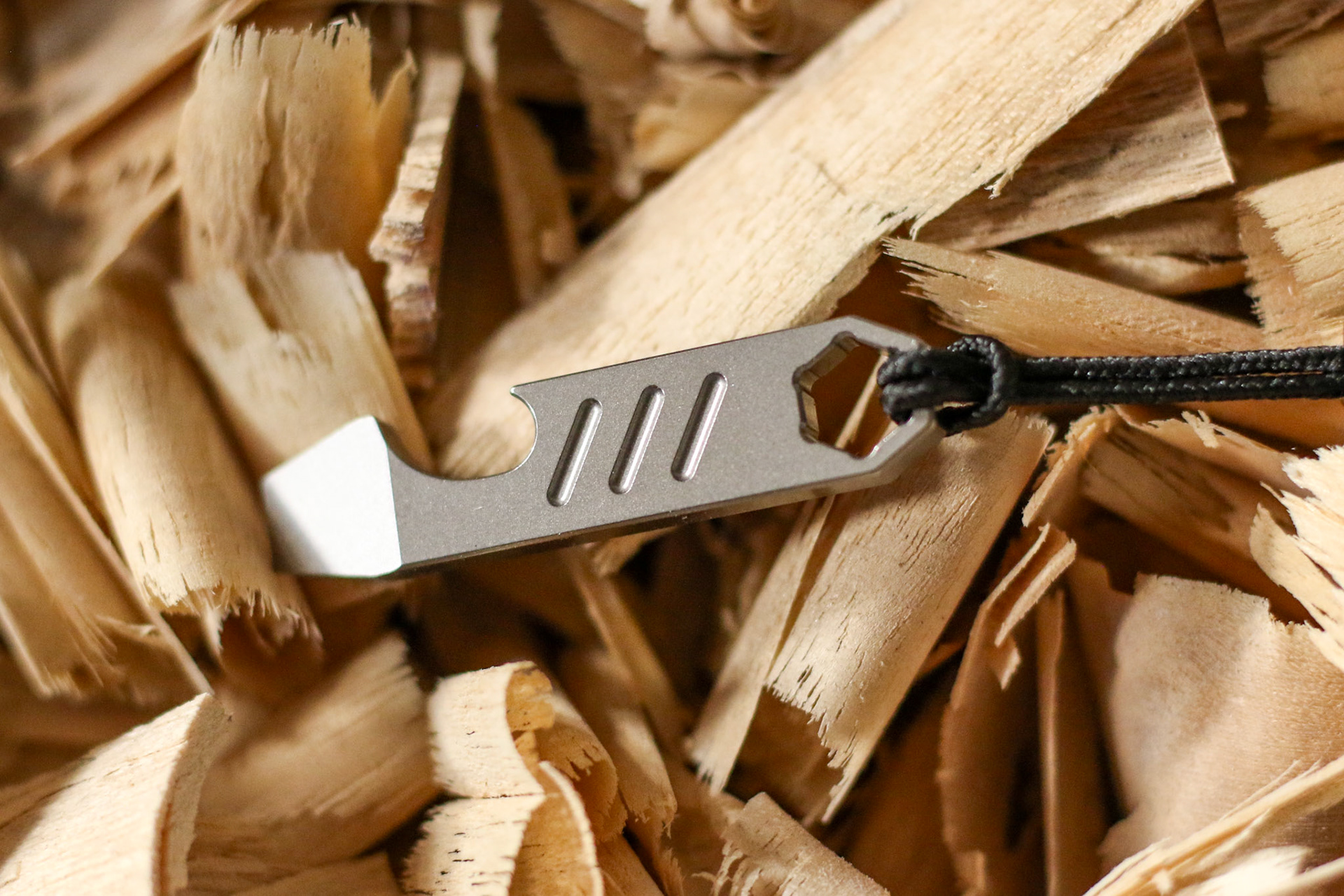 Titanium prybar resting among wood shavings with lanyard attached