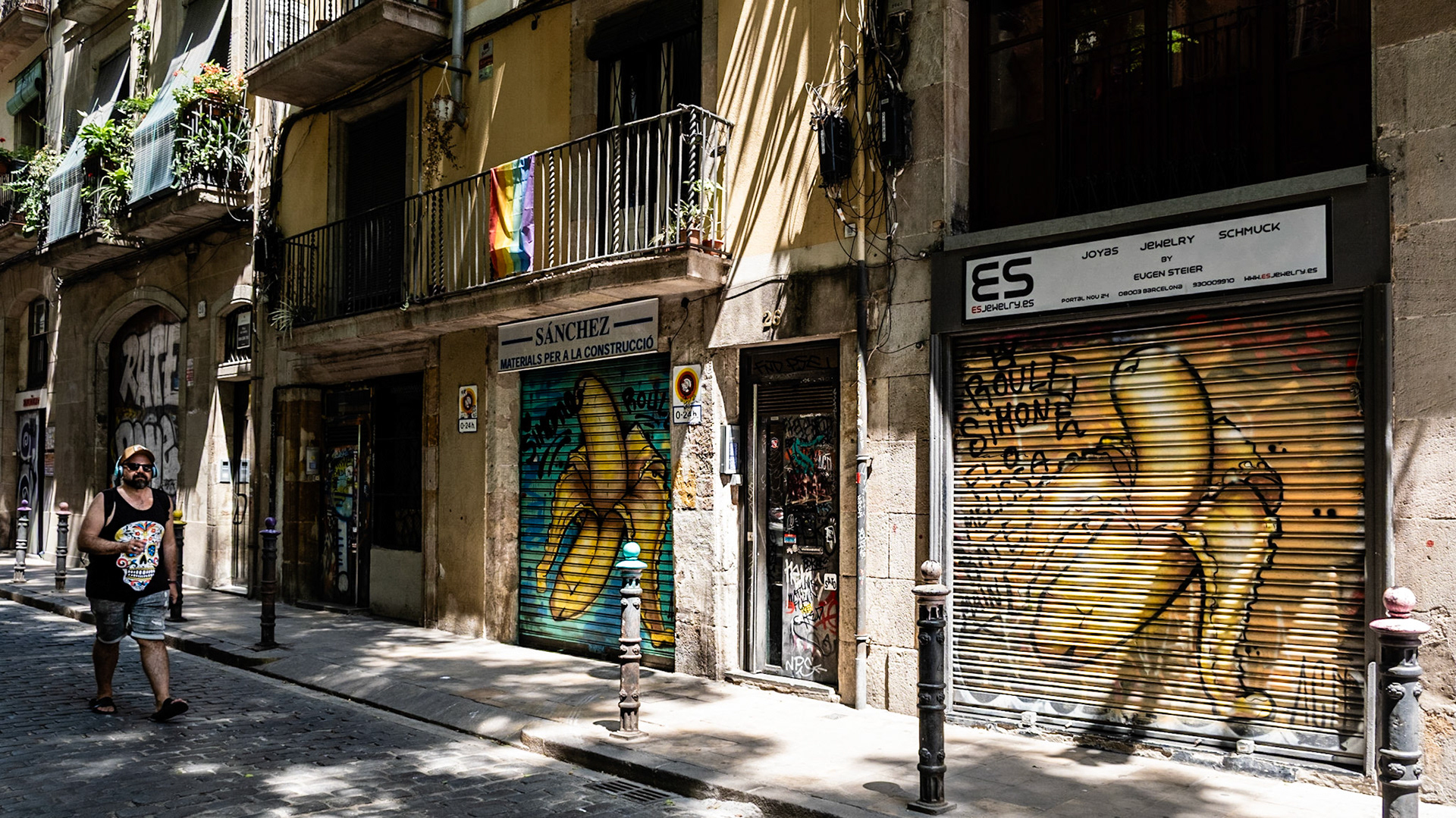 A man walks on a cobblestone street in Barcelona with buildings scarred by graffiti