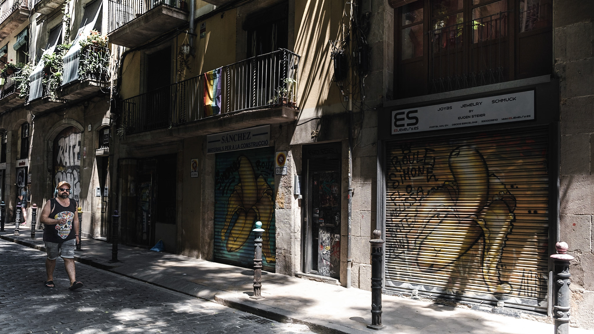 A man walks on a cobblestone street in Barcelona with buildings scarred by graffiti