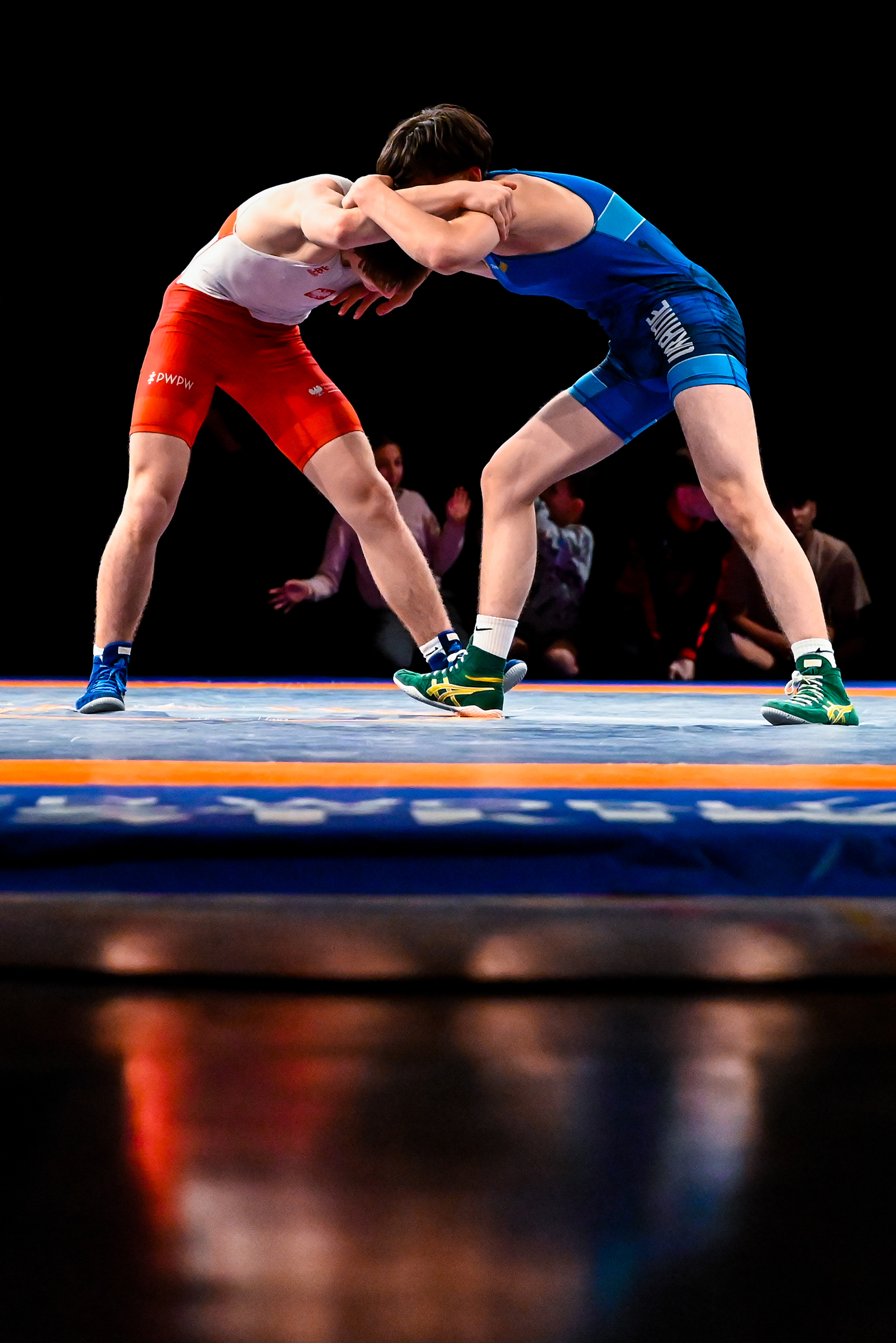Two male youth wrestlers in red and blue singlets engage in a standing collar tie during a freestyle wrestling match at Frem Cup 2026 in Randers, Denmark, under dramatic arena lighting at an international youth tournament.