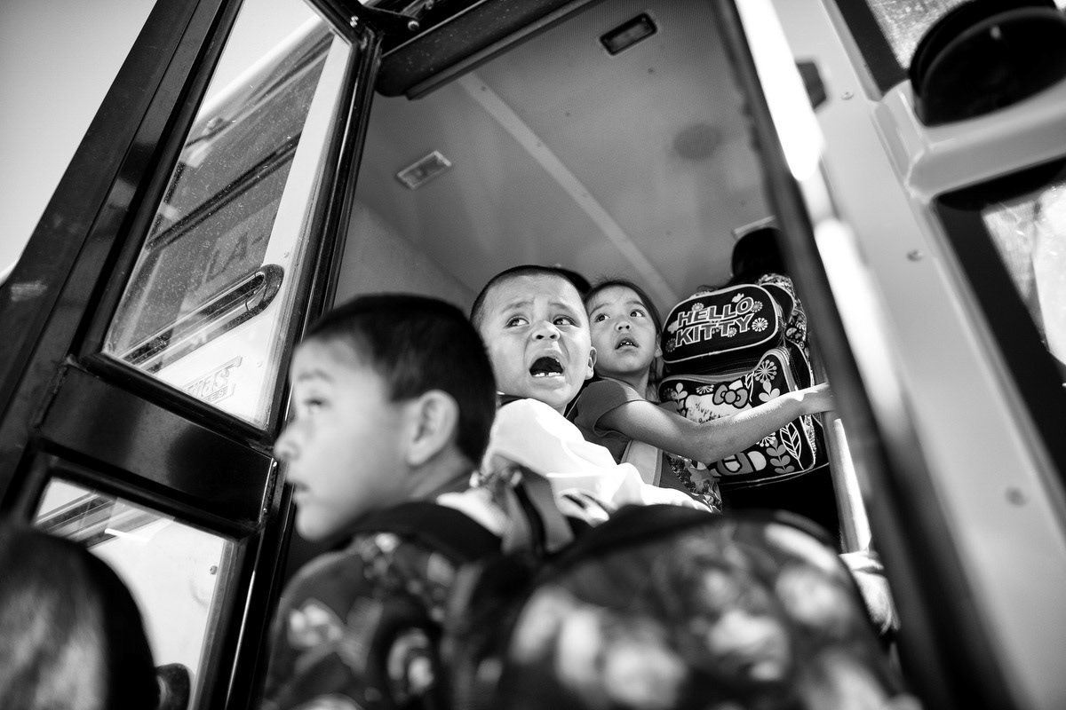Children respond to a teacher while boarding a bus.
