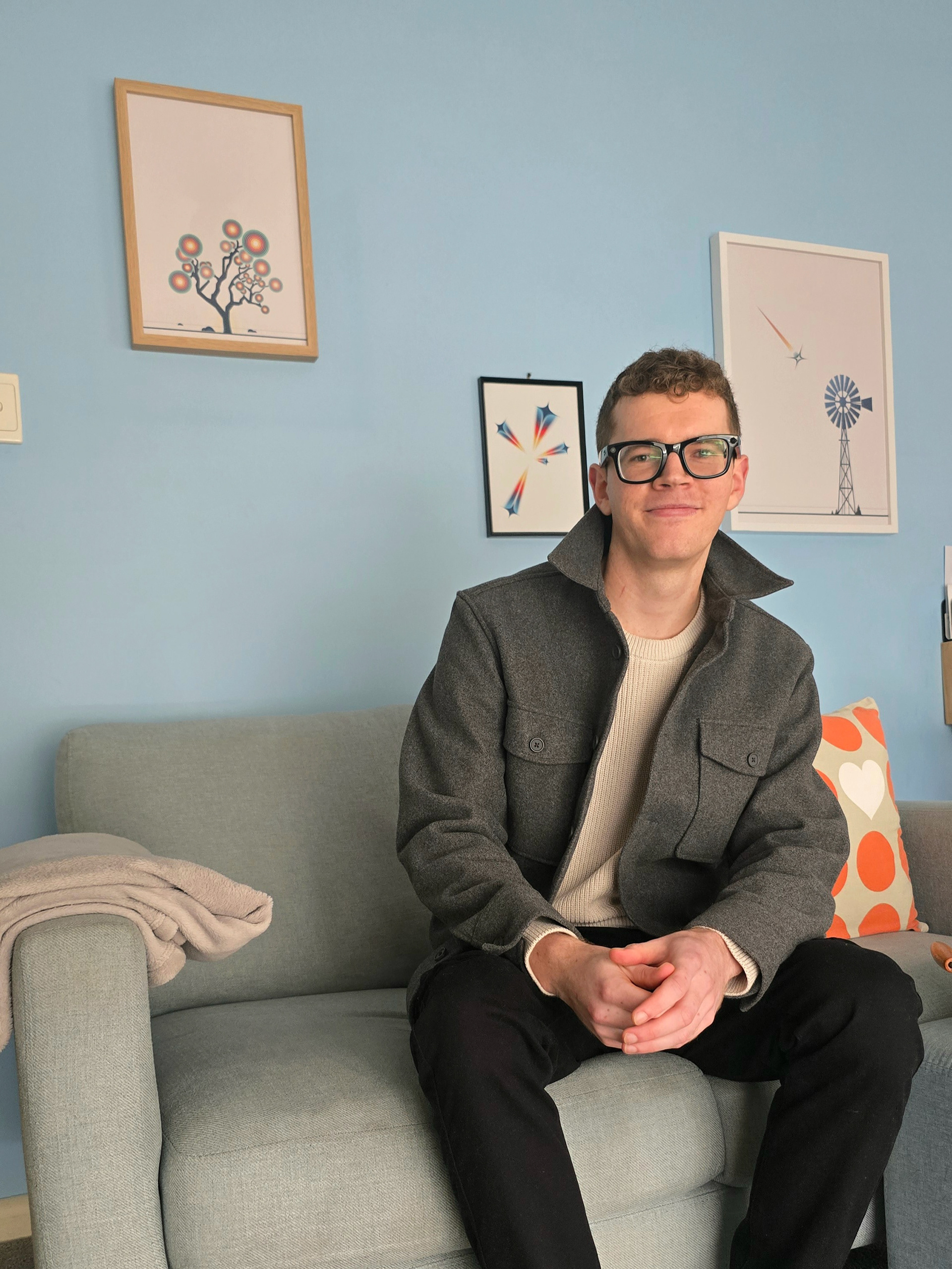 Headshot of the artist, LX, sitting on a couch in a minimalist interior with two of his geometric art prints on the wall.