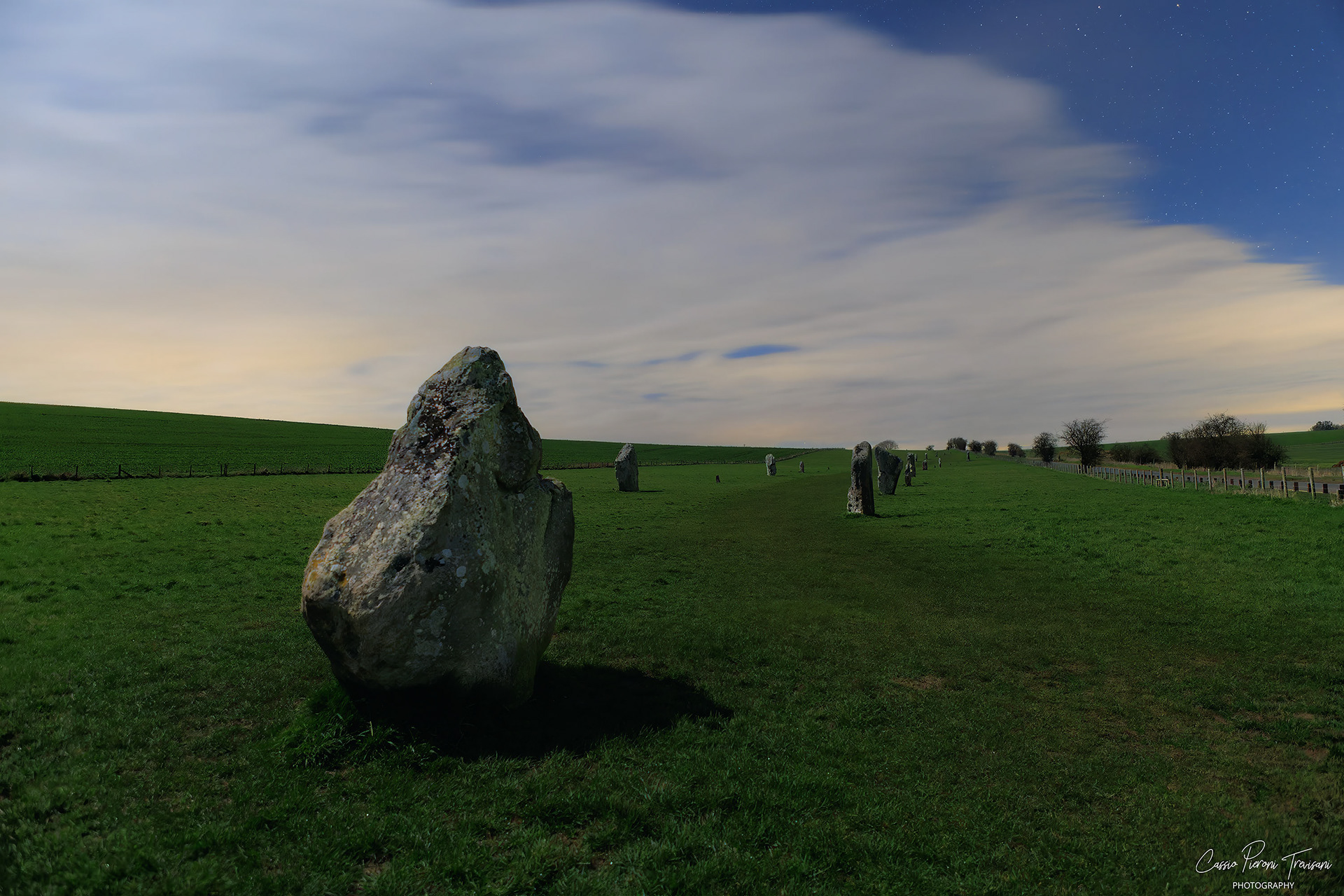 The ancient avenue recedes into darkness, guiding the eye through the landscape as clouds drift across the night sky in long exposure.