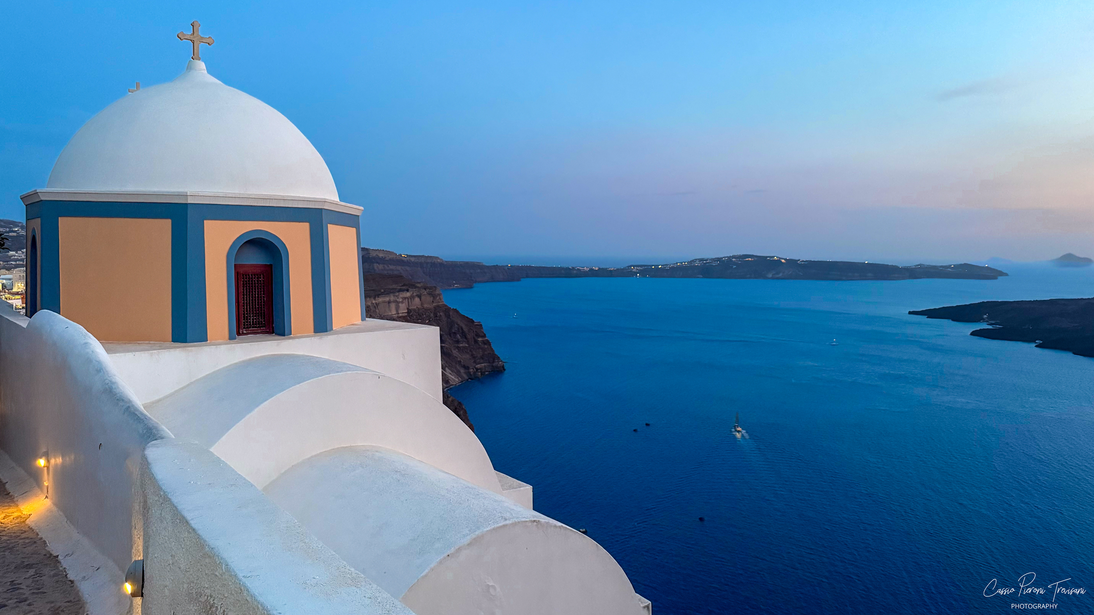 A quiet moment at dusk as a chapel stands above the calm waters of the caldera.