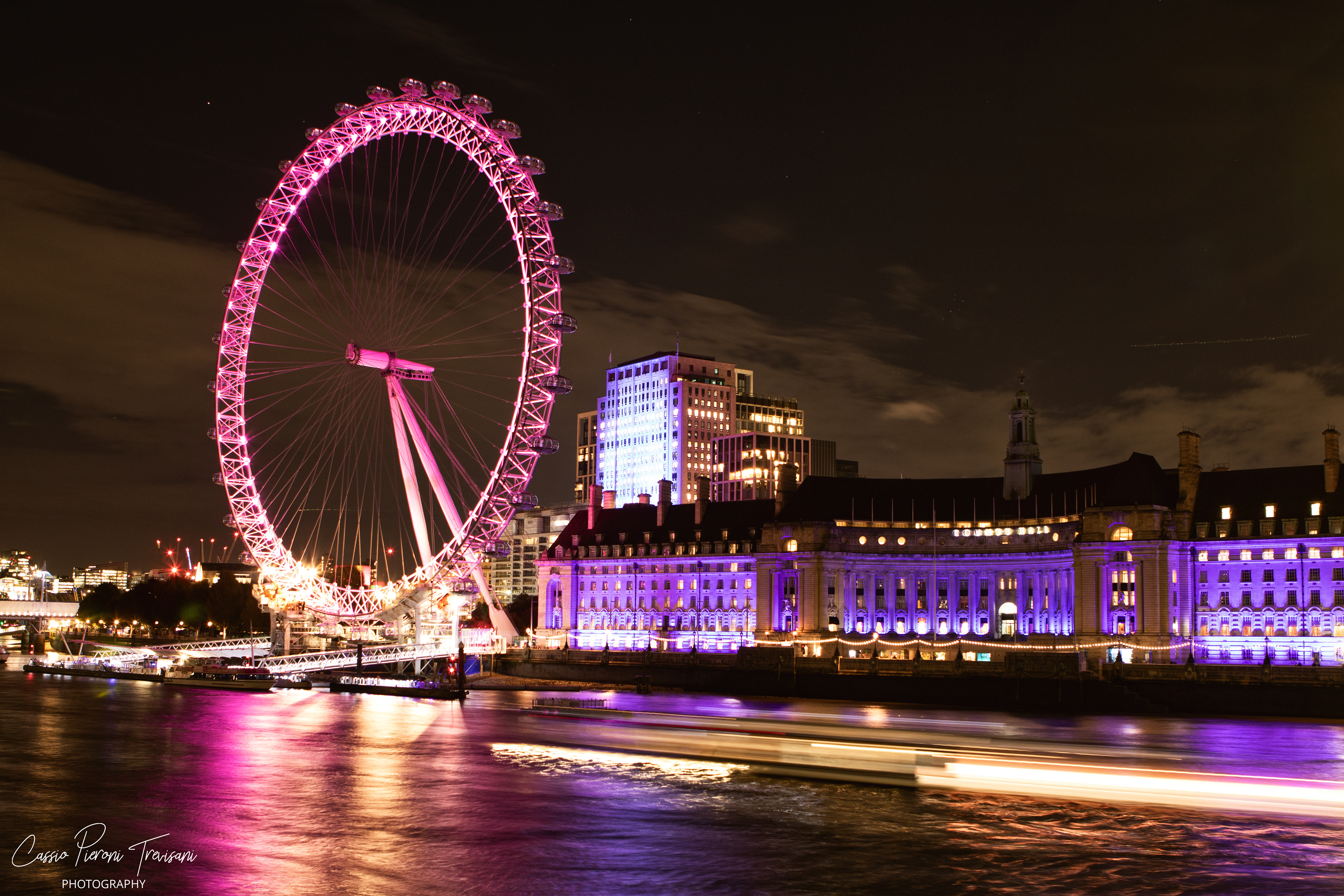 The London Eye rises in luminous magenta while light trails sweep across the Thames, capturing London in motion through long exposure.
