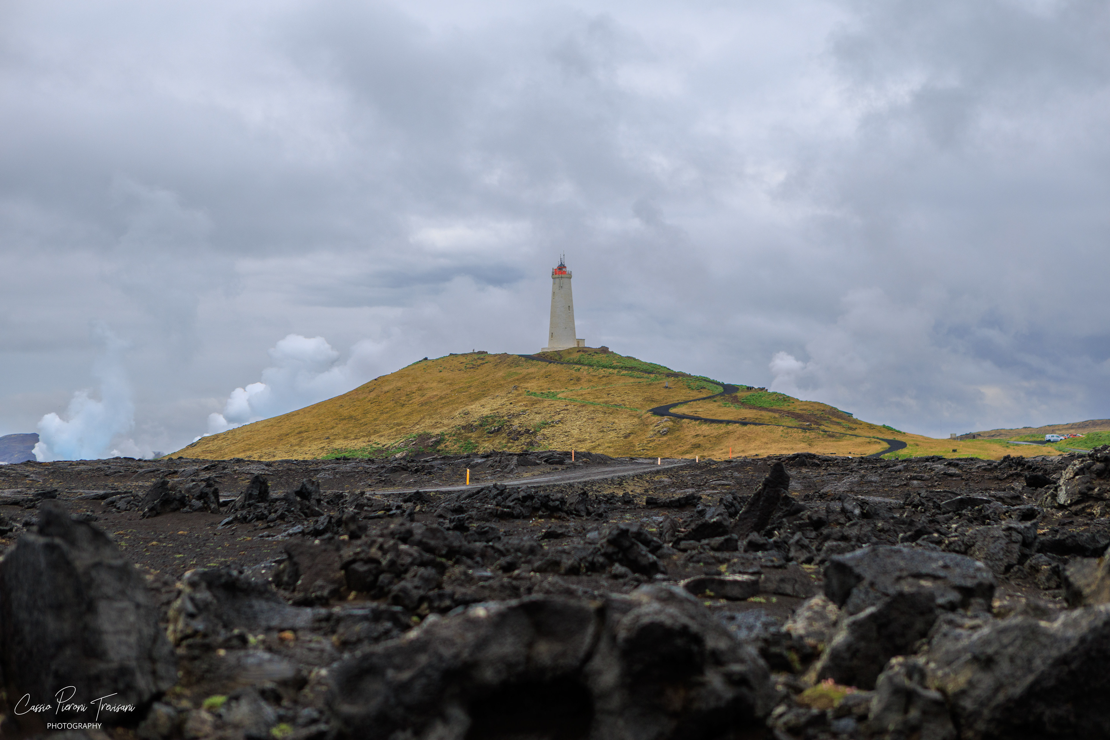 Reykjanesviti Lighthouse rises from a grassy hill beyond the black lava field, standing watch over Iceland’s windswept southwestern coast.