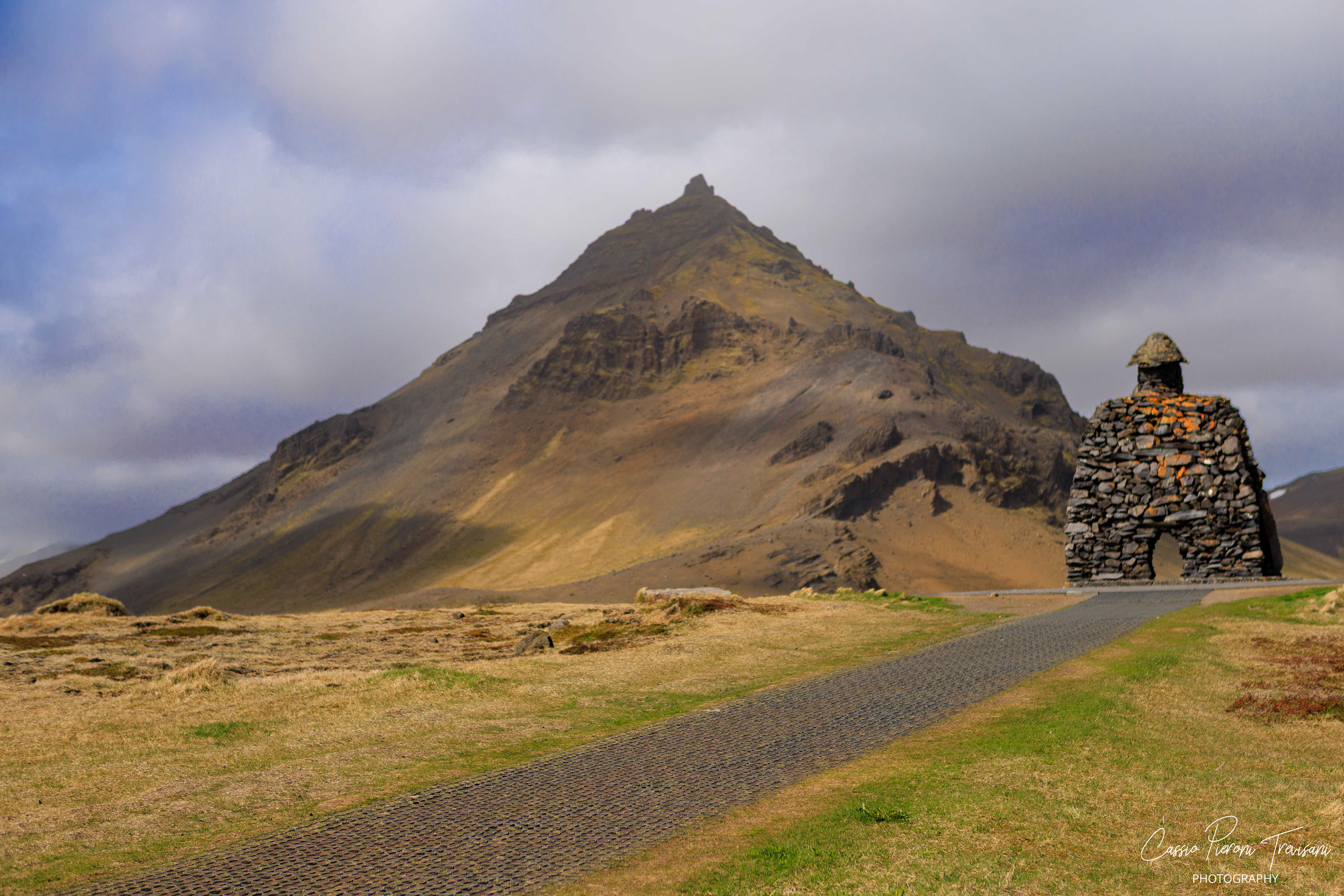 A dramatic mountain rises behind the stone guardian (Bárður Snæfellsás), where Icelandic myth and volcanic landscape meet under a moody sky.