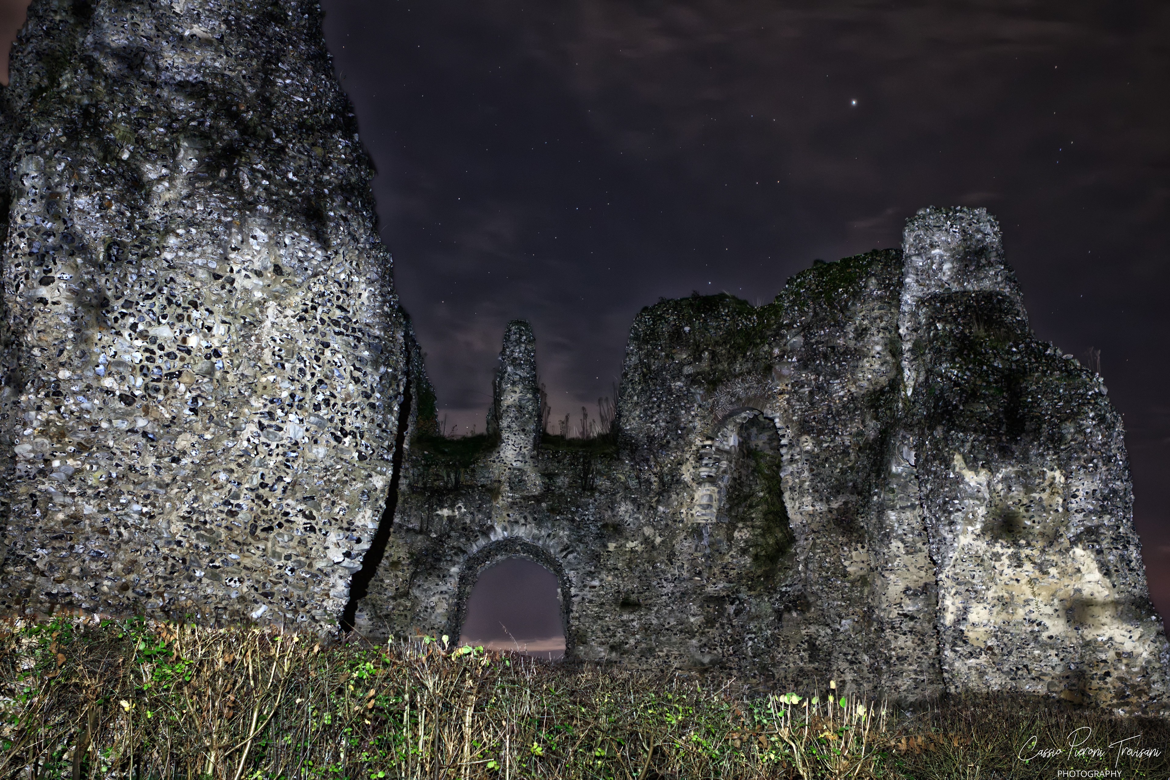 Nighttime photograph of Odiham Castle ruins, highlighting tall fragmented walls and an arched opening.