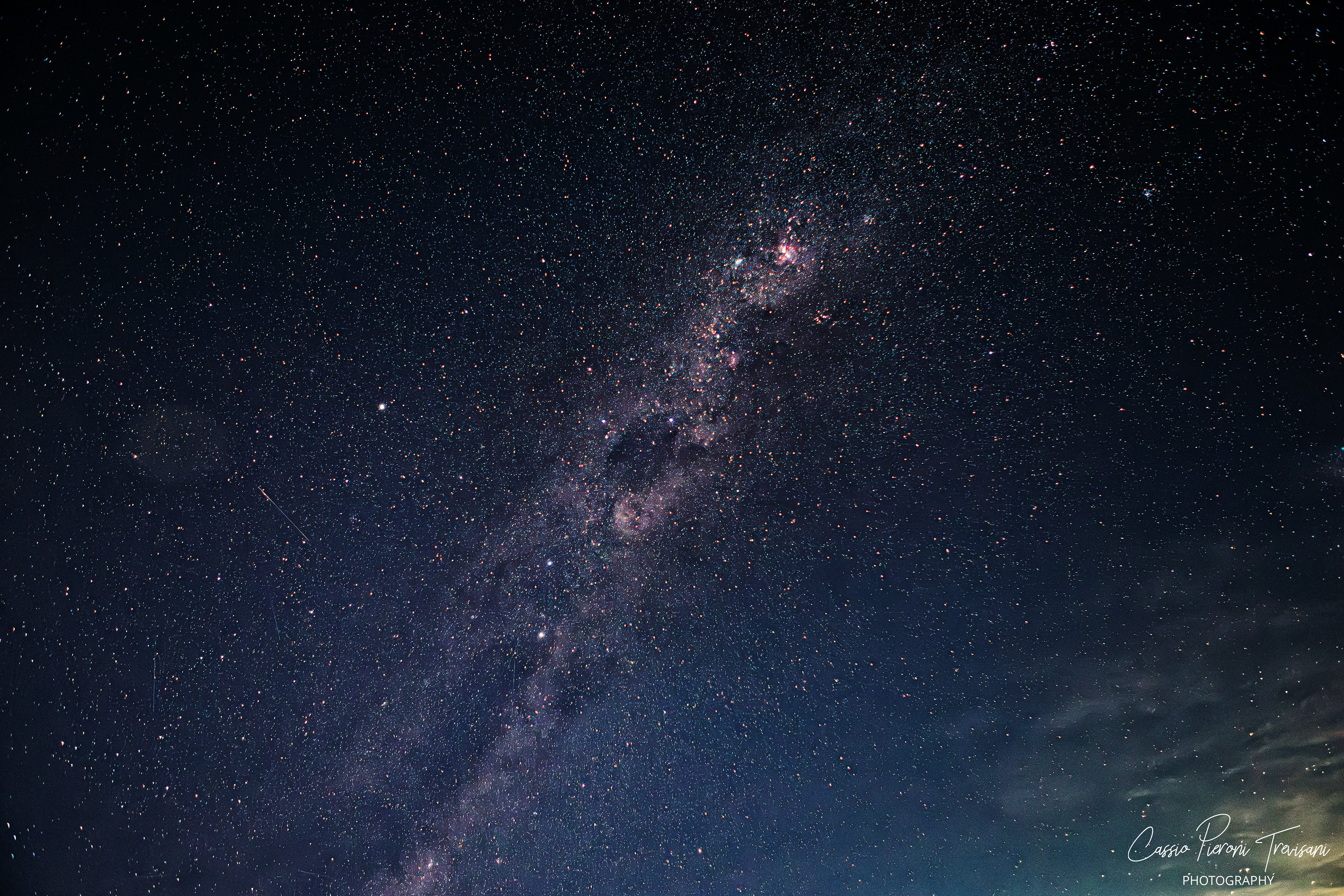 The Milky Way stretches diagonally across a deep, star-filled night sky above rural Minas Gerais, revealing dense star clouds and glowing nebulae in pristine darkness.
