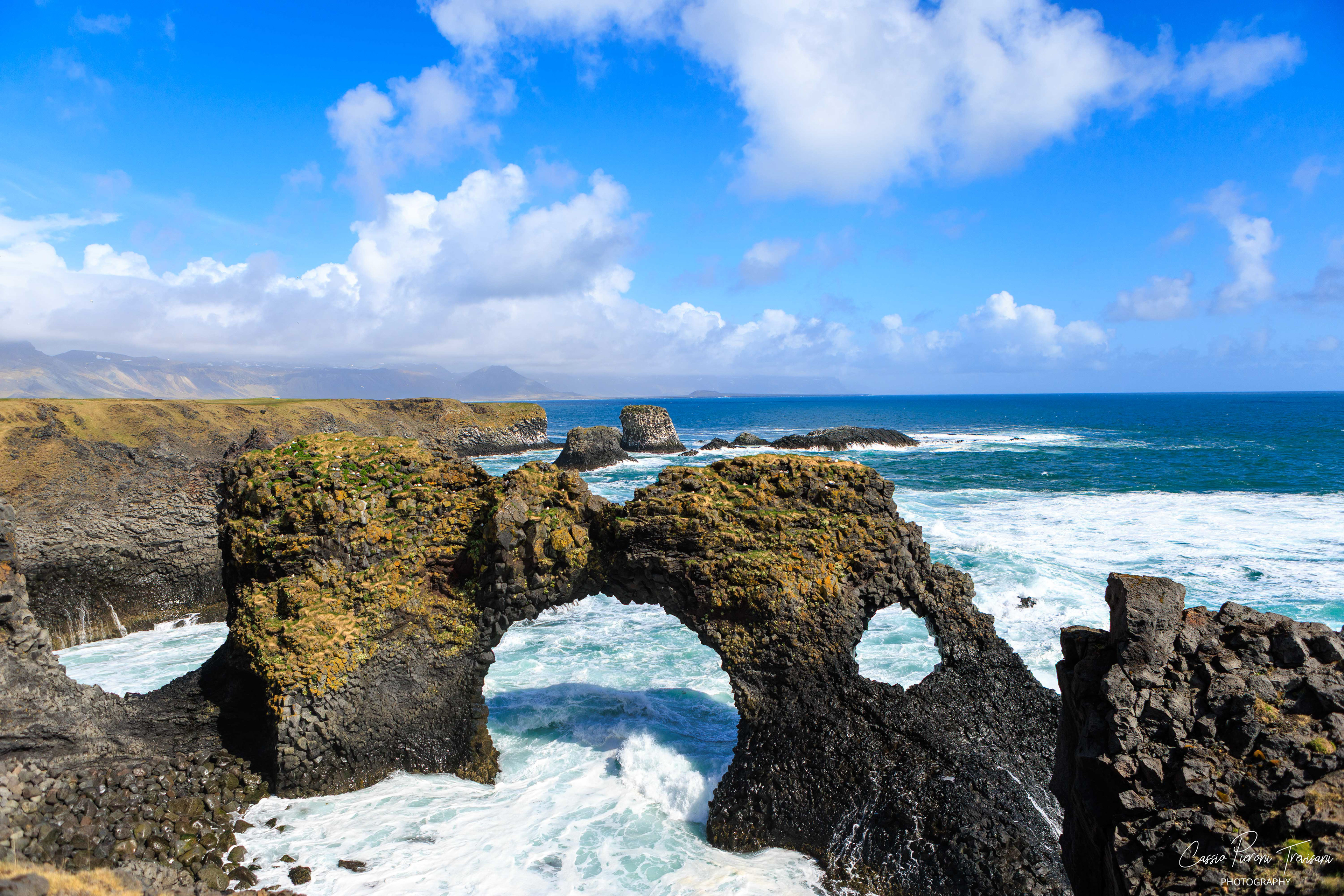 Waves crash beneath a natural lava arch, revealing the power of the ocean against Iceland’s rugged volcanic coastline.