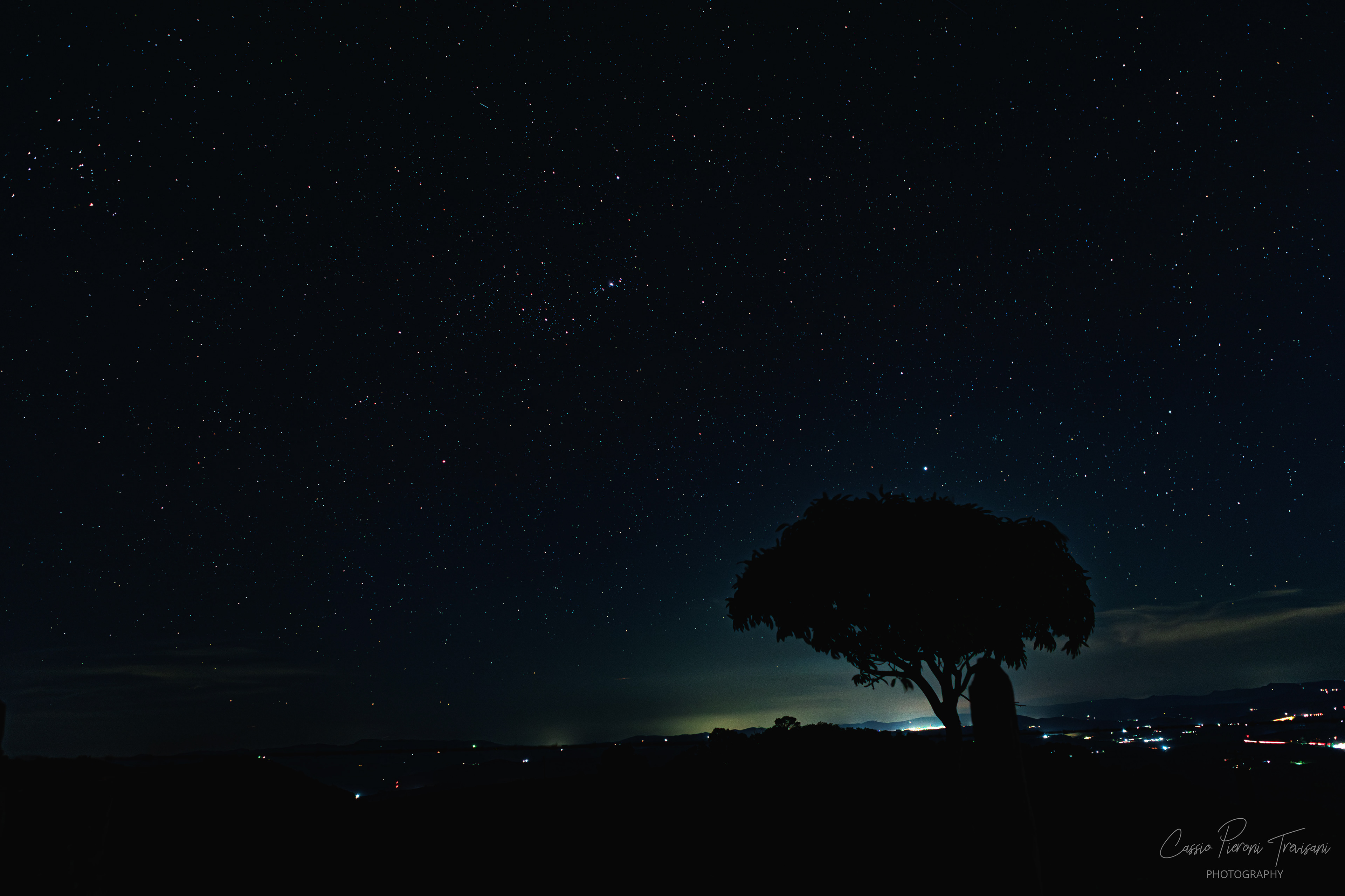 Star-filled night sky over rural Jacutinga with a silhouetted tree and distant lights.