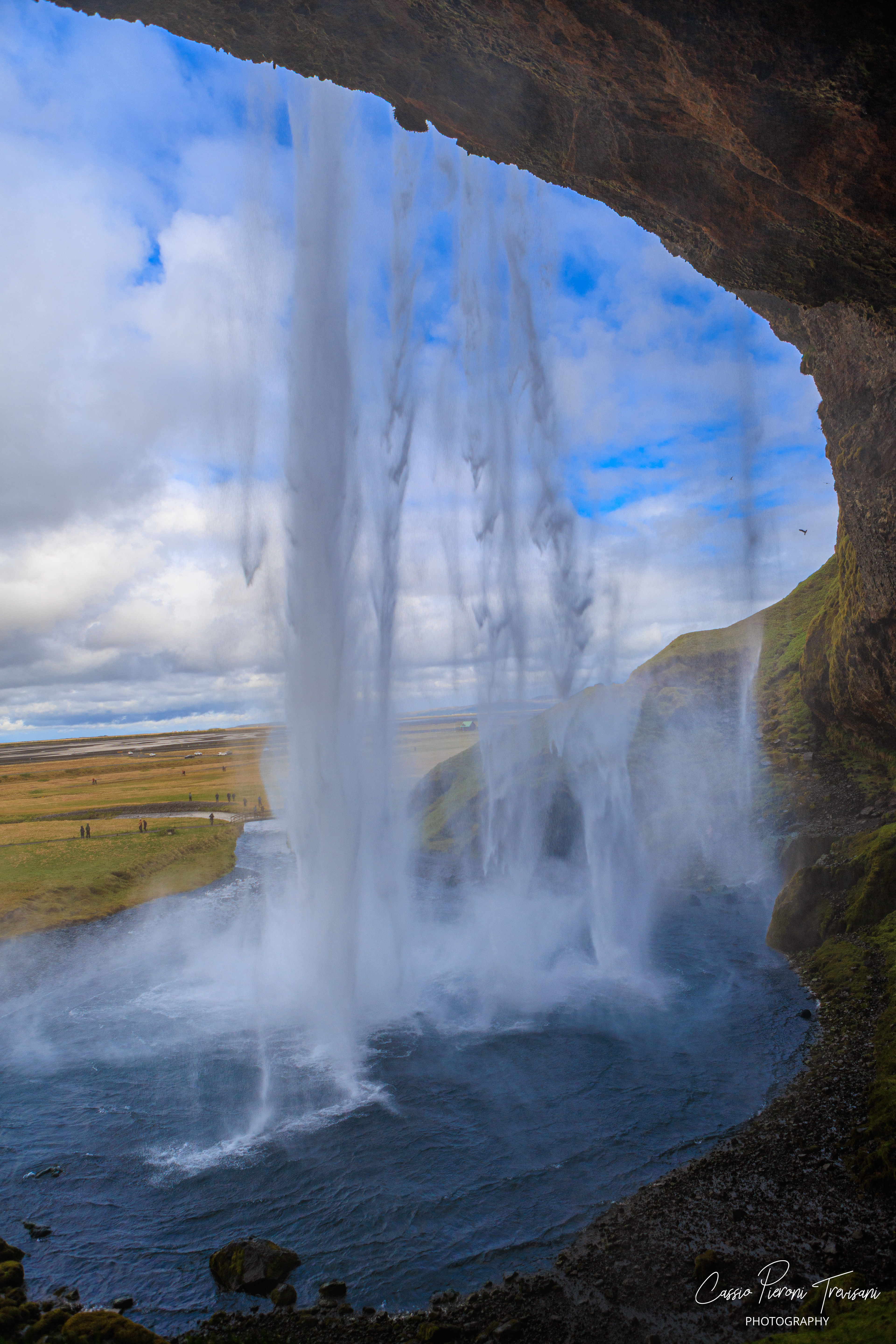 Looking outward from behind the falls, the landscape appears through a translucent veil of water and spray..