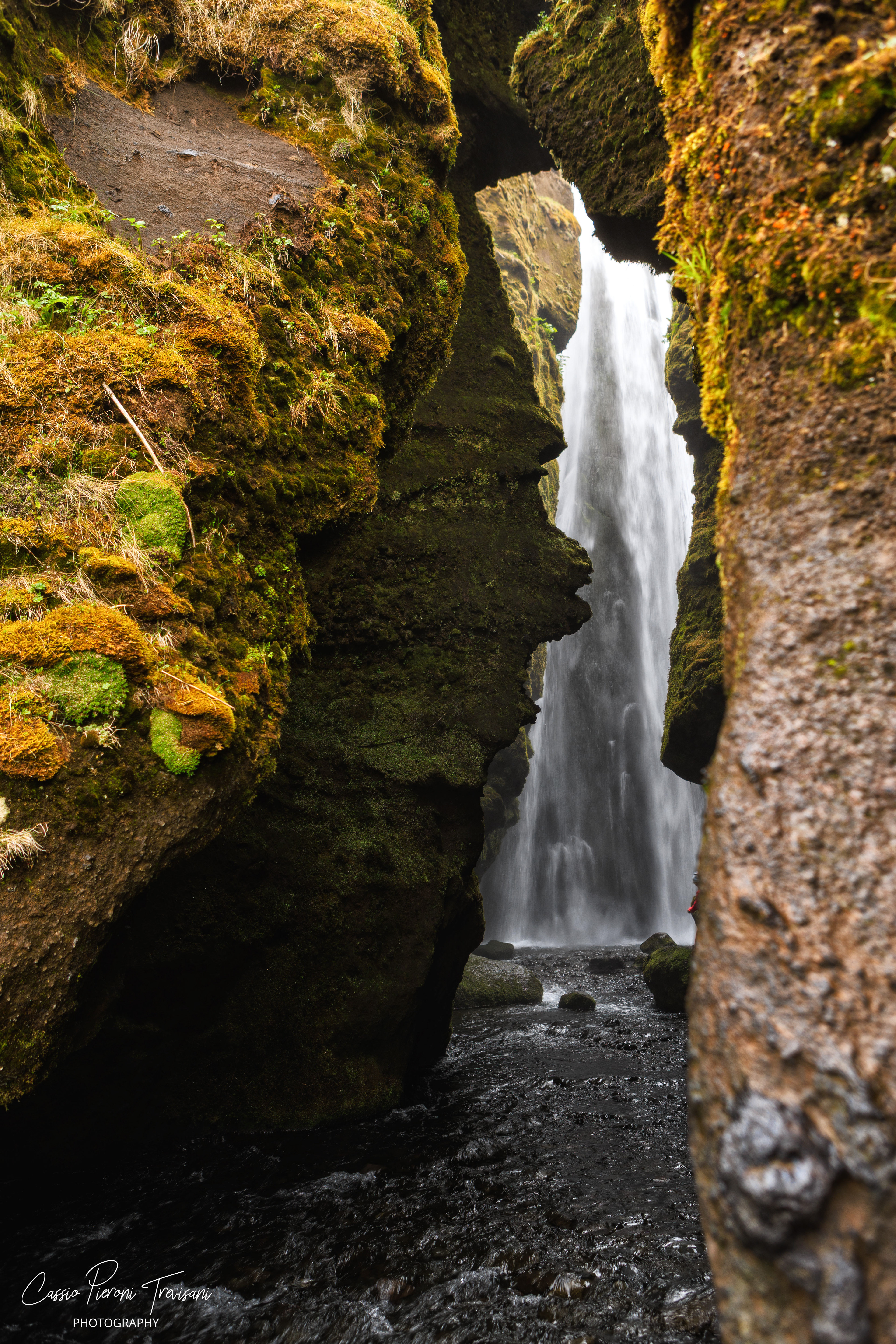 Gljúfrabúi appears through a narrow mossy canyon, hidden between dark rock walls and flowing water.