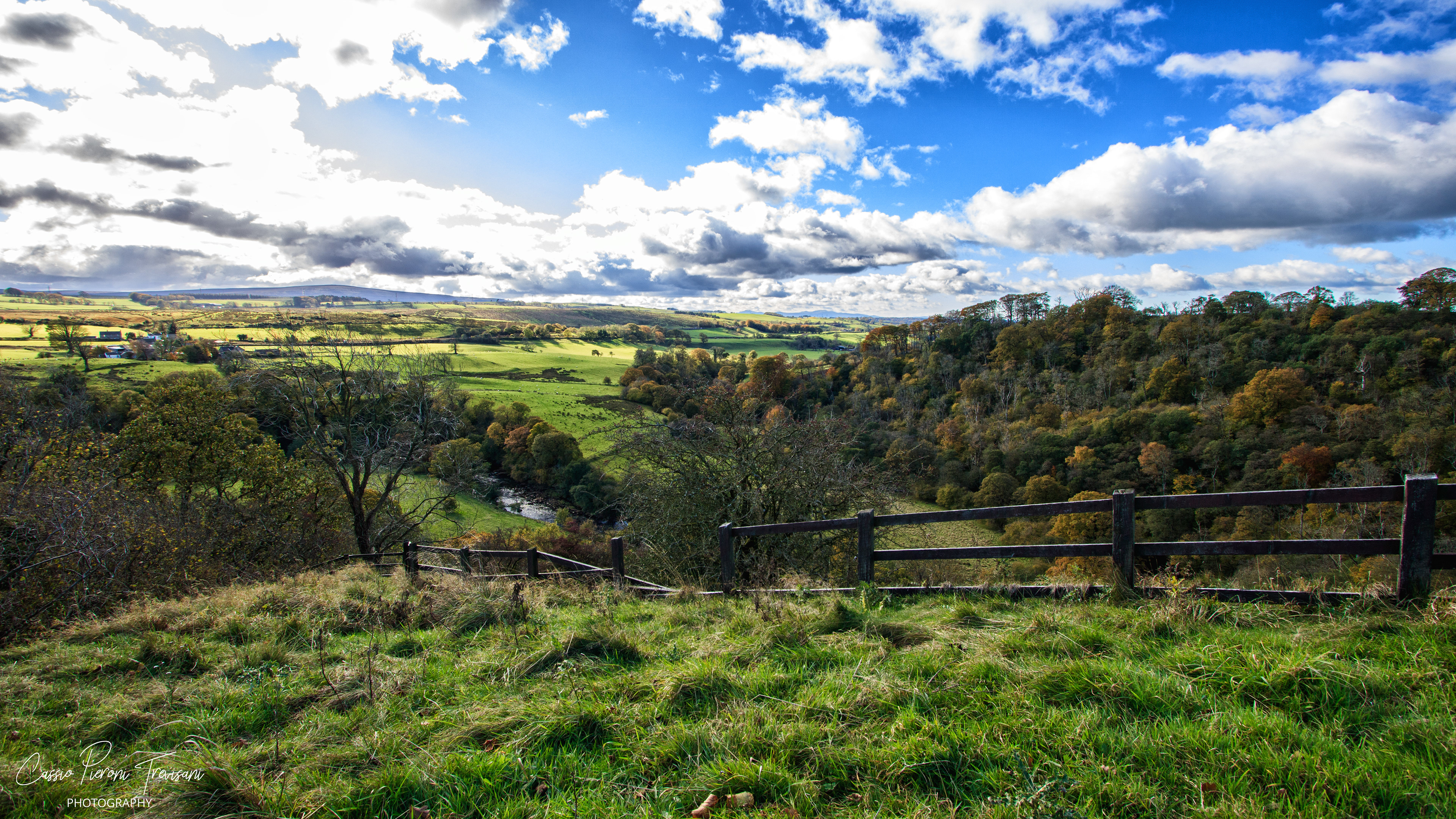 A sweeping view across the Northumberland valley, where sunlight breaks through passing clouds to illuminate the patchwork landscape below.