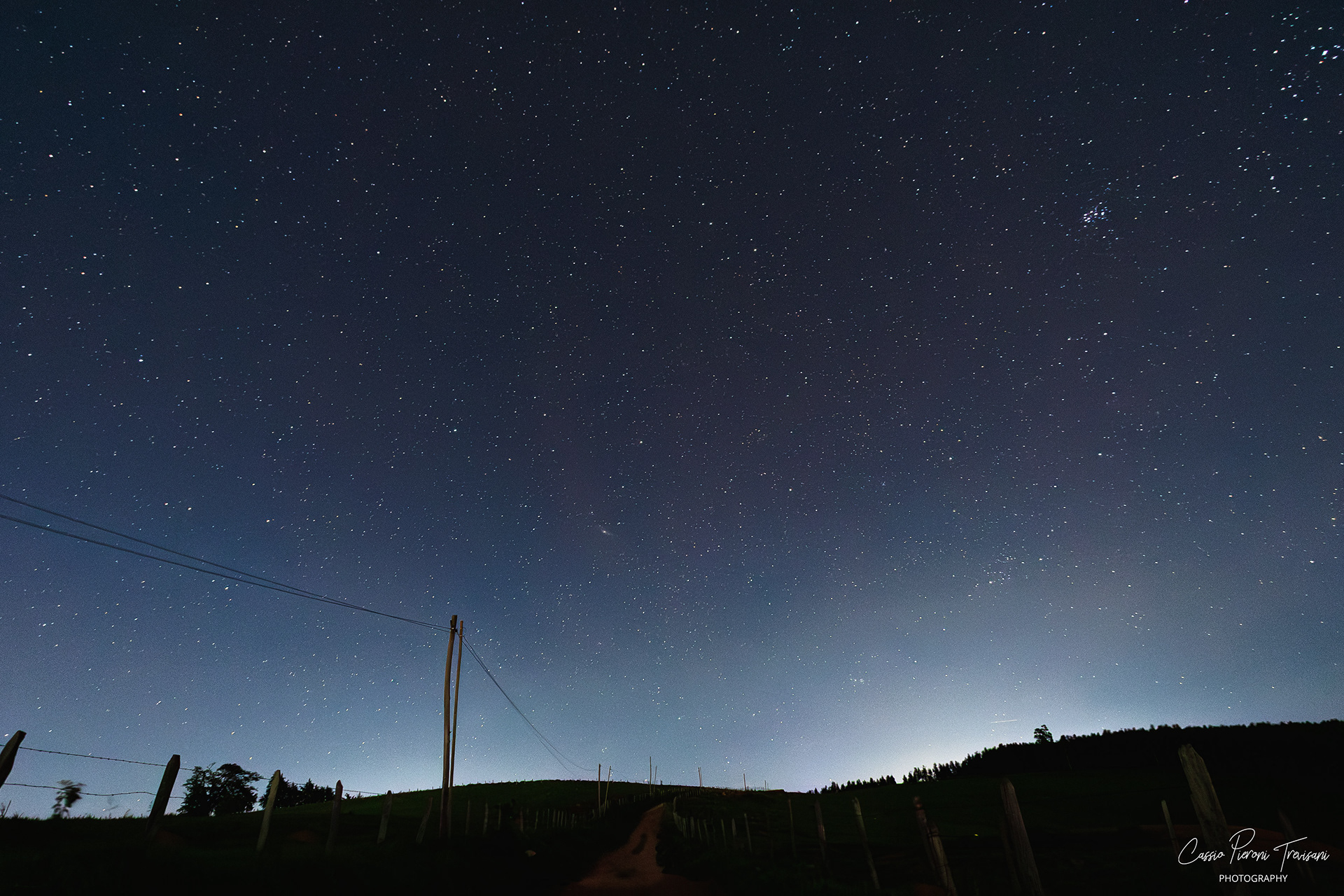 Deep night sky over Jacutinga with distant city glow and fence posts.