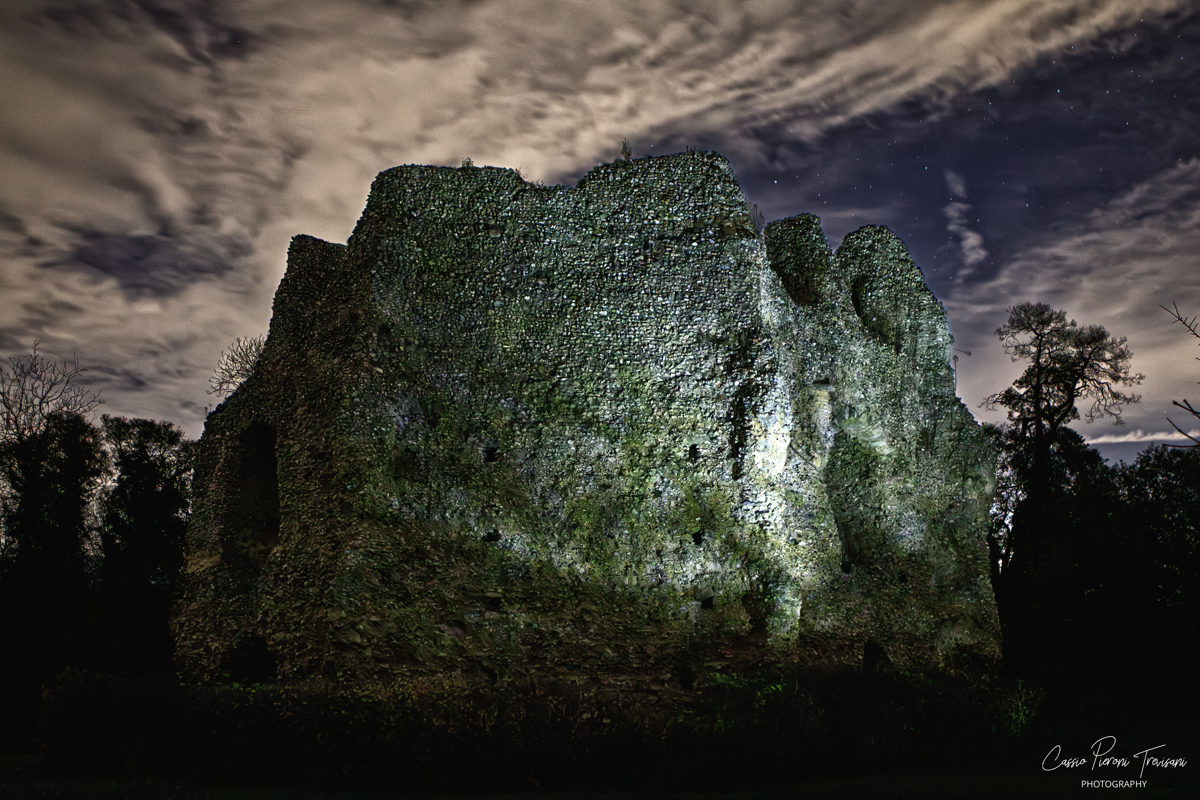 Night view of Odiham Castle’s large stone ruin illuminated against a cloudy, star-filled sky.