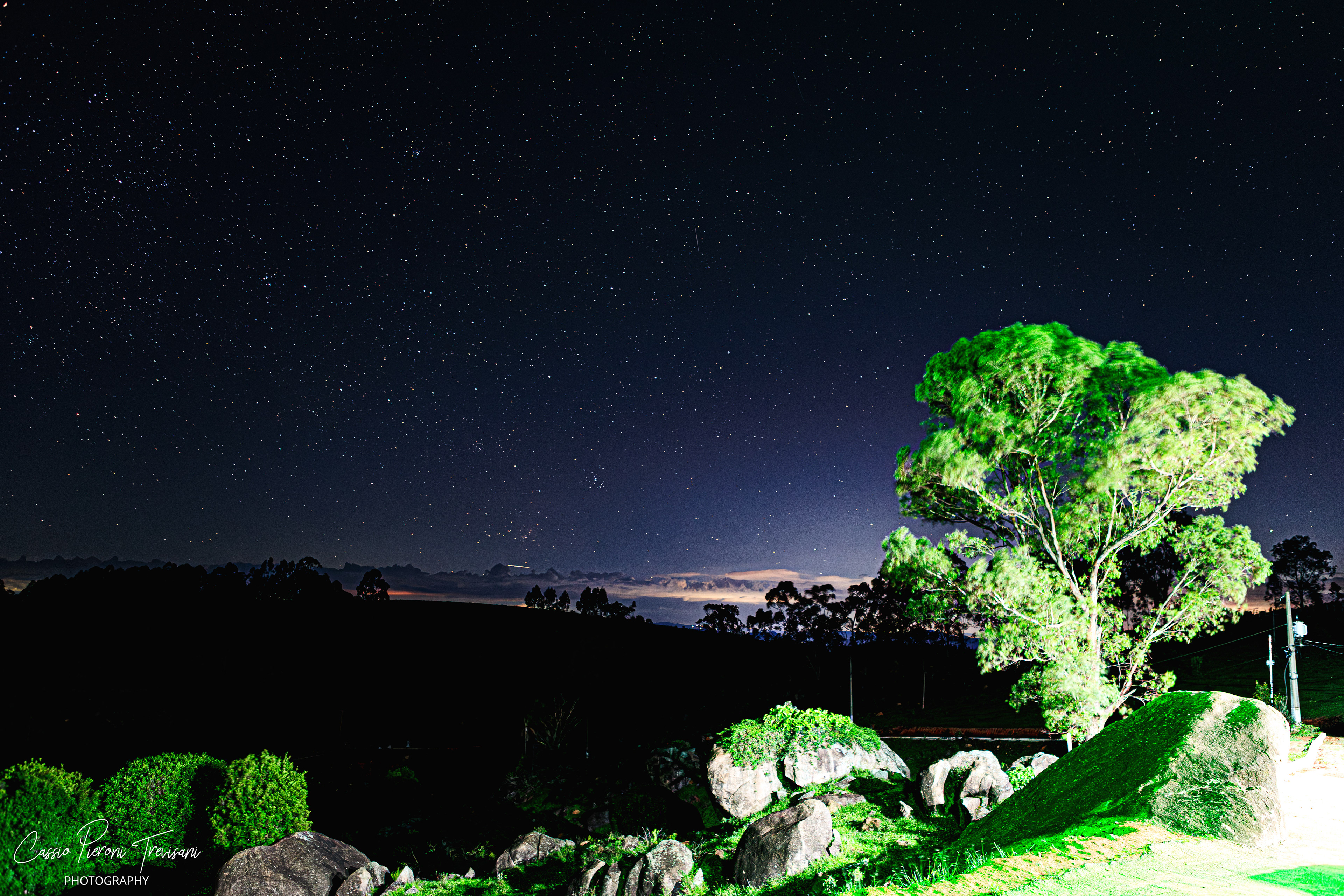 Starry sky over Mirante de Albertina with illuminated foreground and distant landscape.