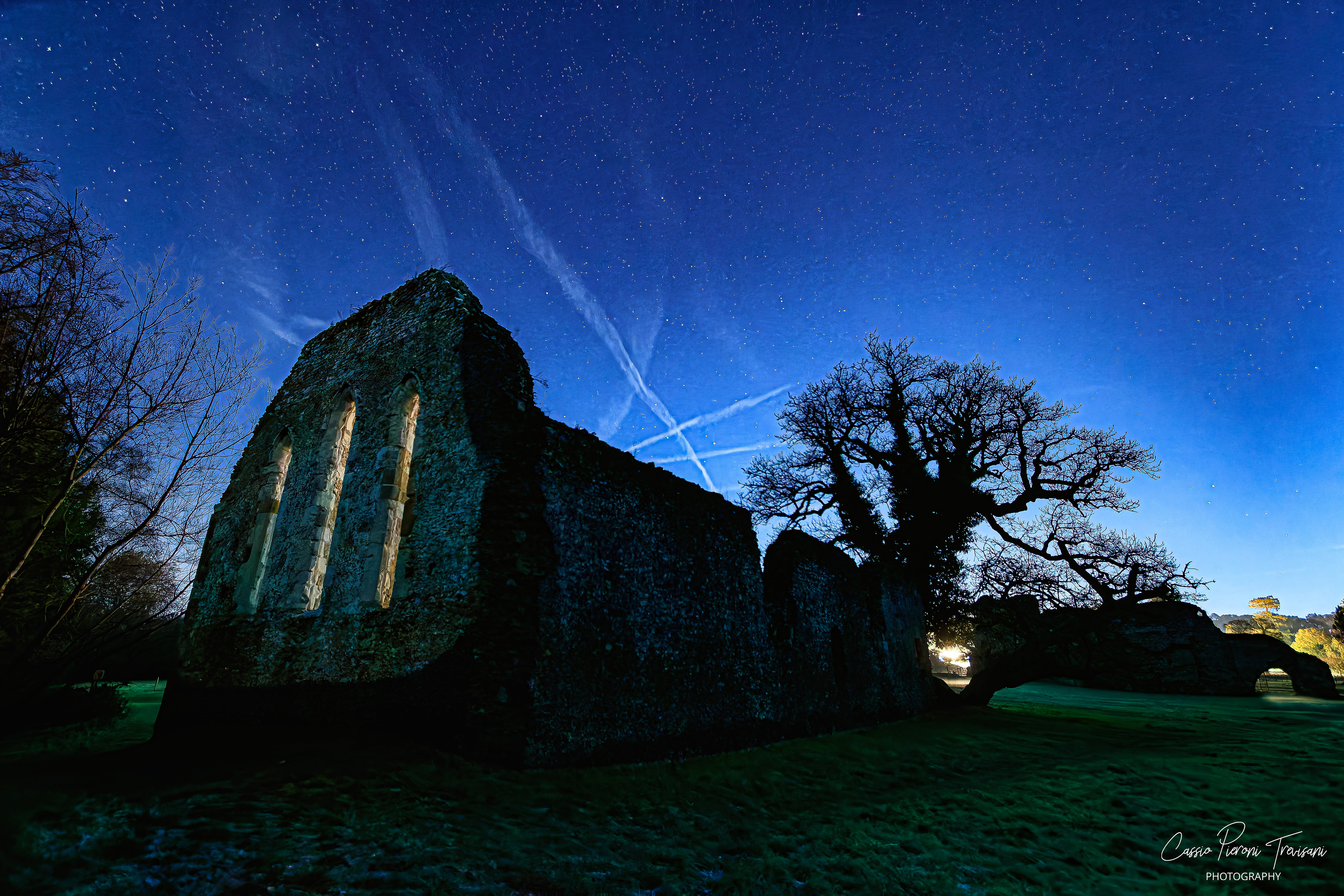Waverley Abbey ruins under a deep blue starry sky with crisscrossing cloud trails.